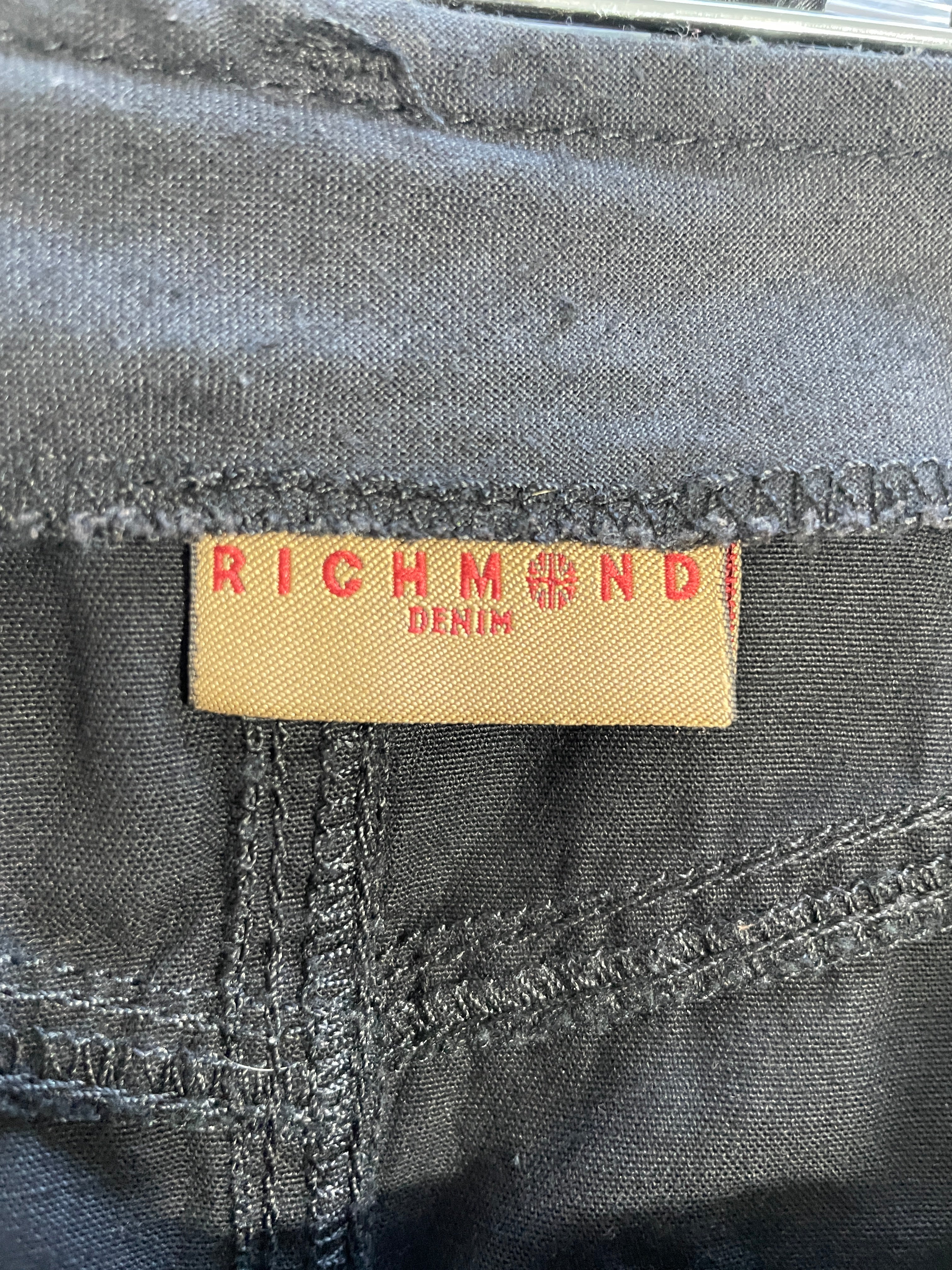 Close-up of a dark gray denim garment showing the interior waistband and a tan fabric brand label that reads RICHMOND DENIM in red lettering.