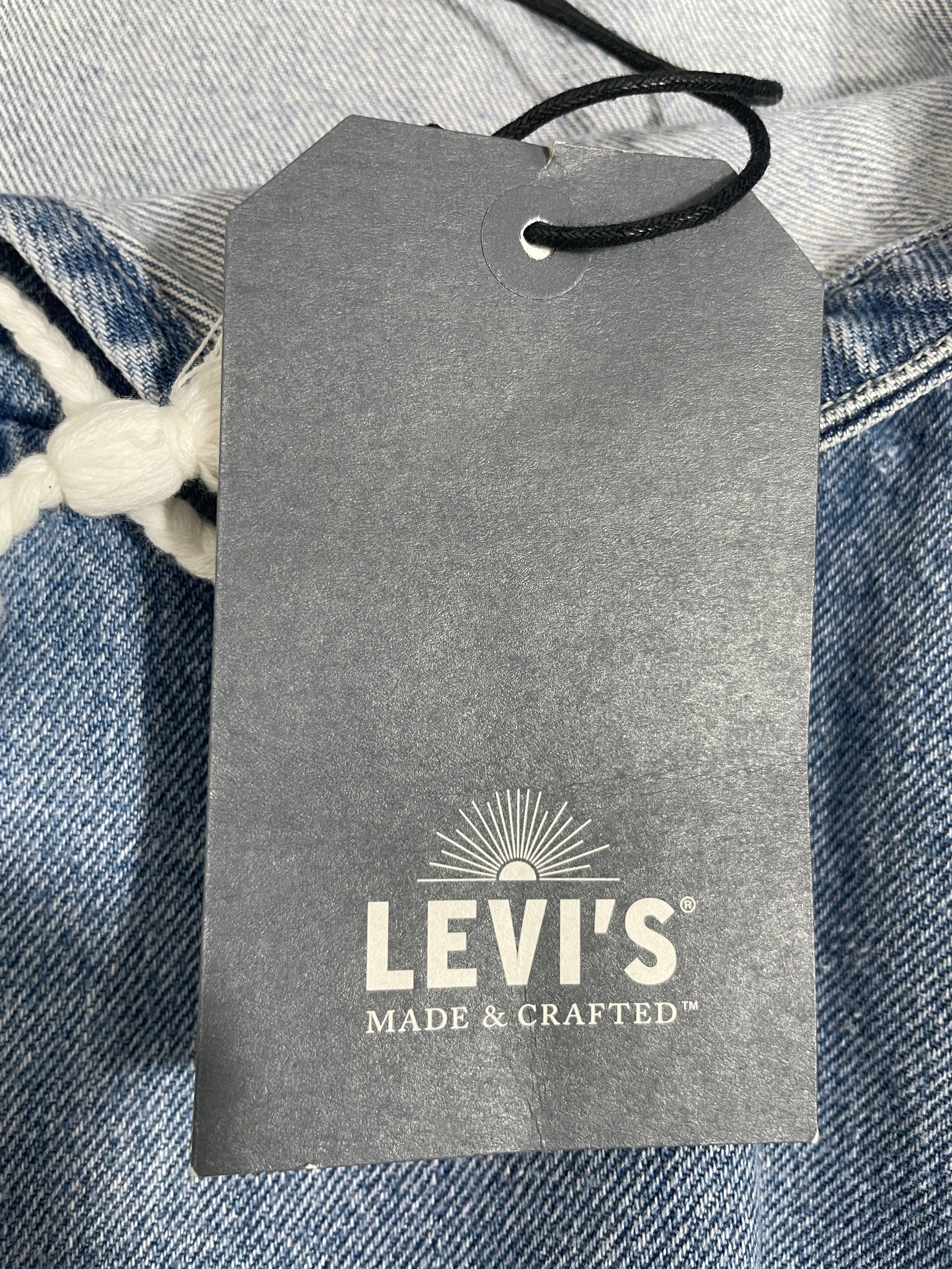 A close-up of a gray Levi's hangtag attached to a pair of blue denim jeans, with the Levi's logo and 'MADE & CRAFTED' text clearly visible.