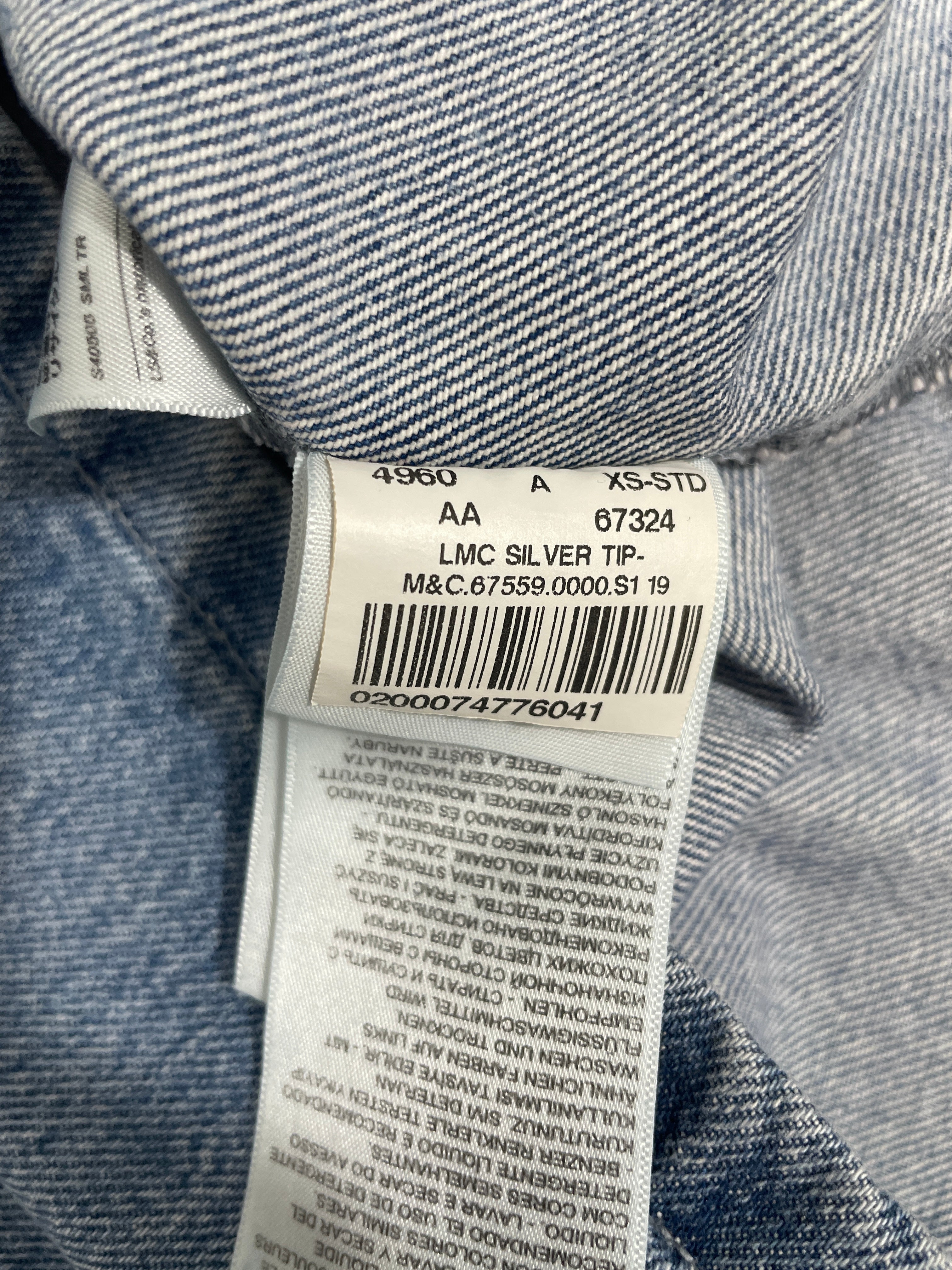 Close-up of a denim garment's inner neck label showing size information, barcode, and care instructions.