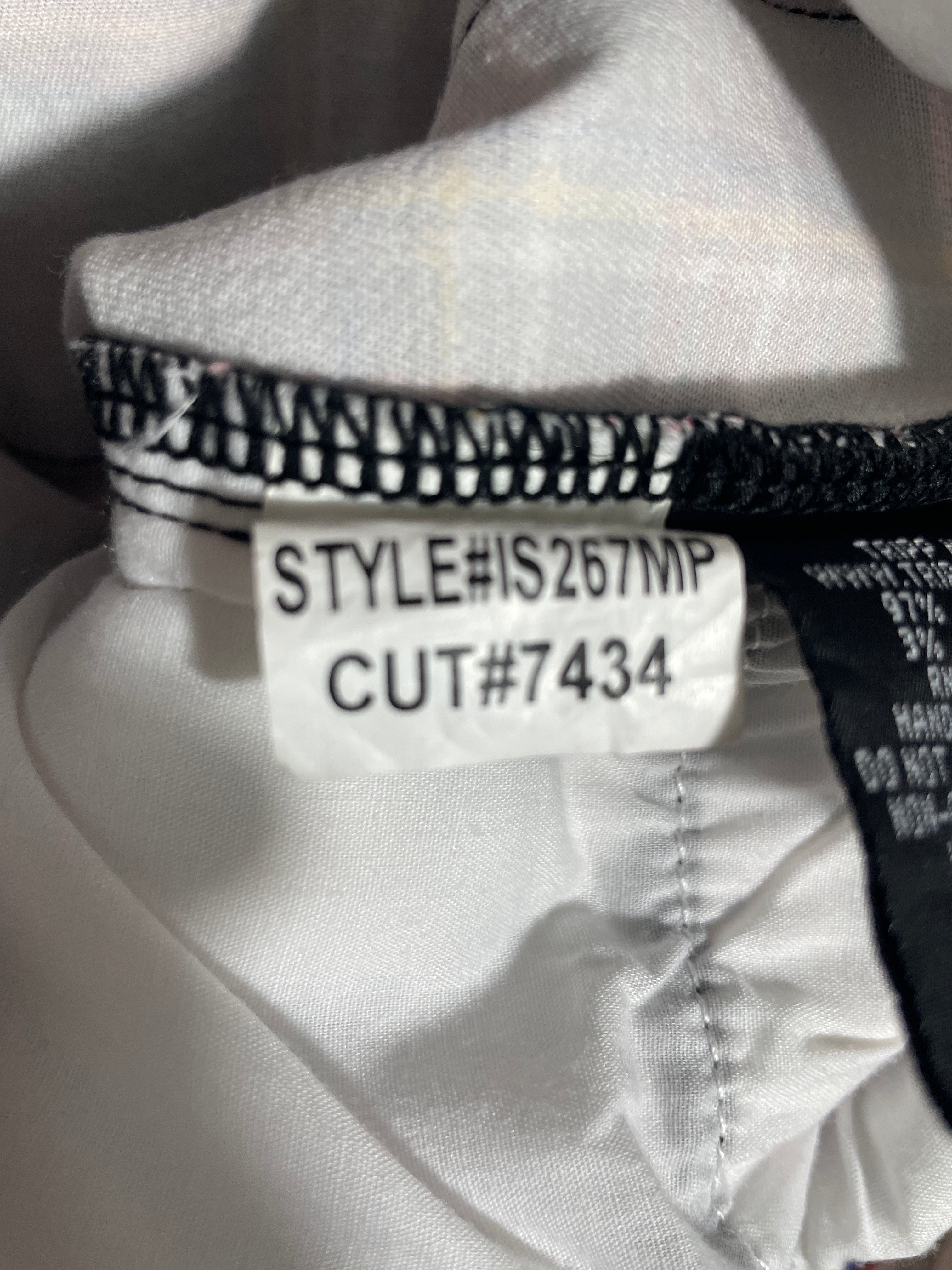 Close-up of a garment's inner neck label showing the style code 'STYLE#IS267MP' and cut code 'CUT#7434' on a white fabric background.