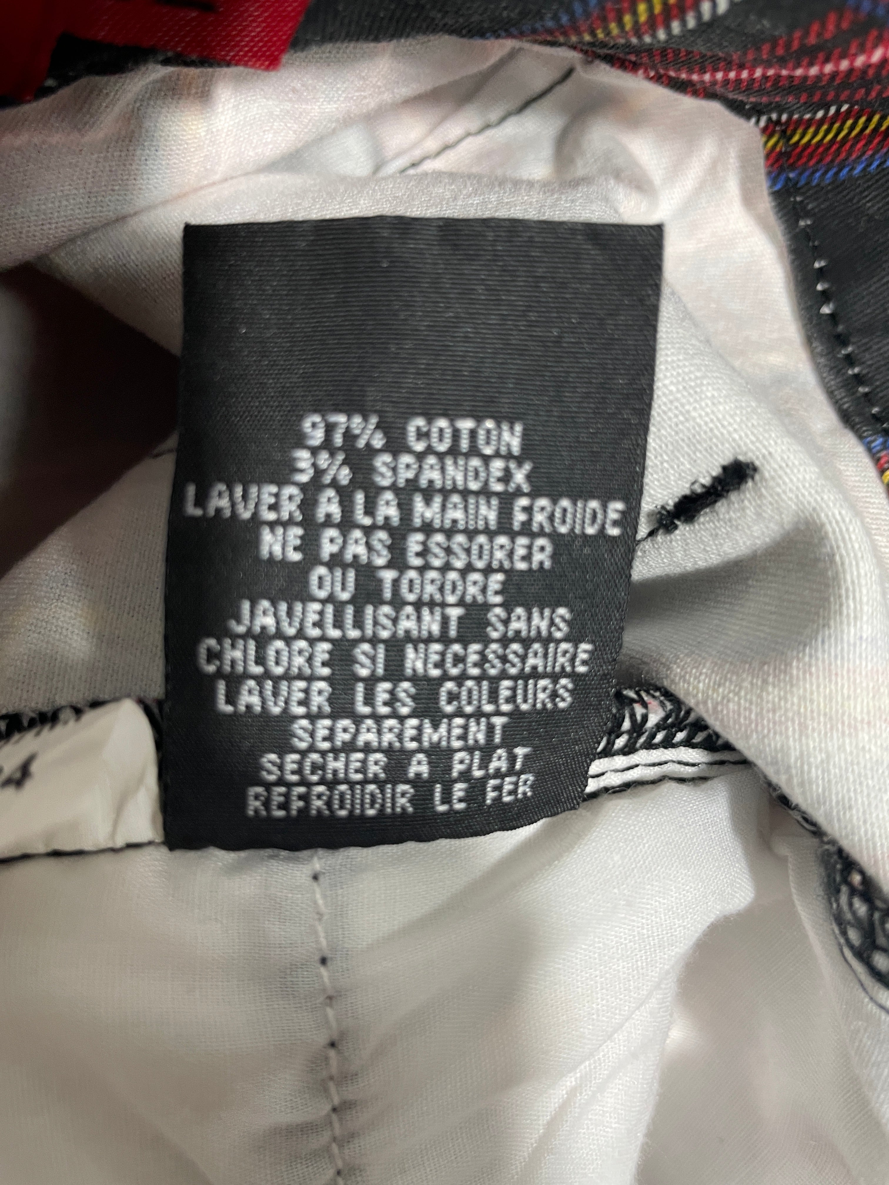 Close-up of a garment's interior label reading '97% COTON 3% SPANDEX LAVER A LA MAIN FROIDE NE PAS ESSORER OU TORDRE JAVELLISANT SANS CHLORE SI NECESSAIRE LAVER LES COULEURS SEPAREMENT SECHER A PLAT REFROIDIR LE FER' on a white fabric background.