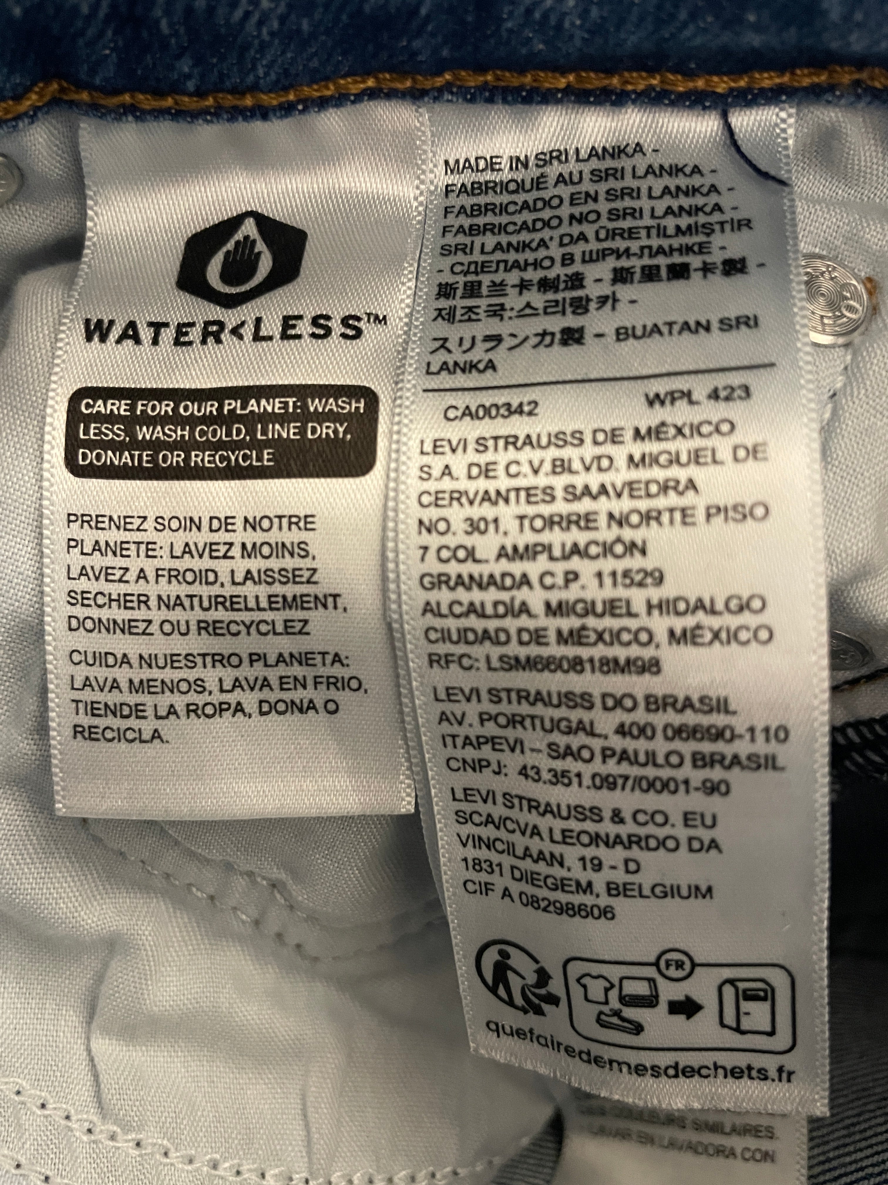Close-up of a sewn-in care and manufacturing label on a white garment. The label reads WATERLESS and shows Made in Sri Lanka, care instructions, product code WPL 423, and multiple brand addresses including Waterless, Strauss de México, Strauss de Brasil, and Strauss & Co.