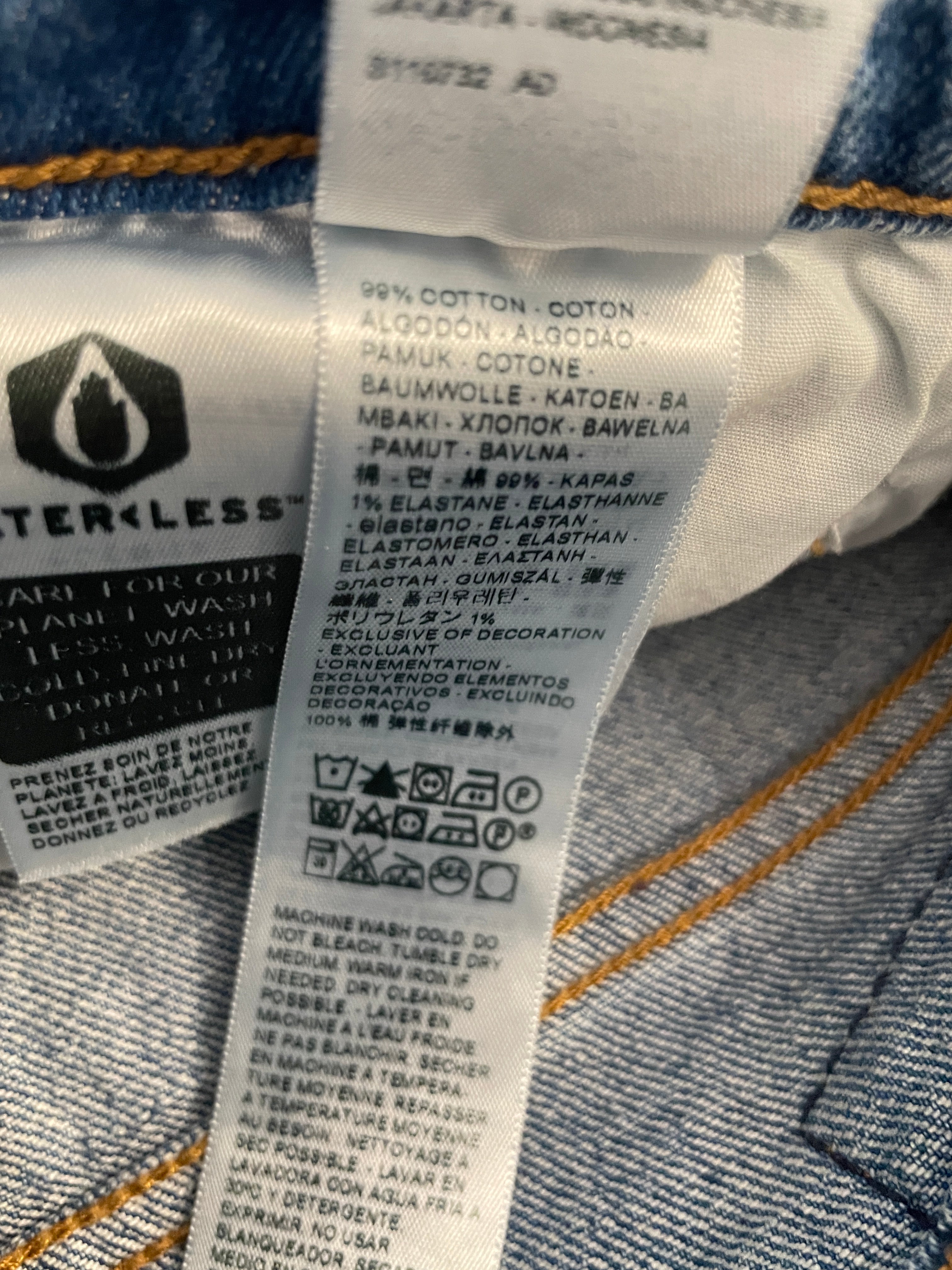 Close-up of a garment care label sewn onto blue denim fabric, showing text including '100% COTTON' and care symbols.