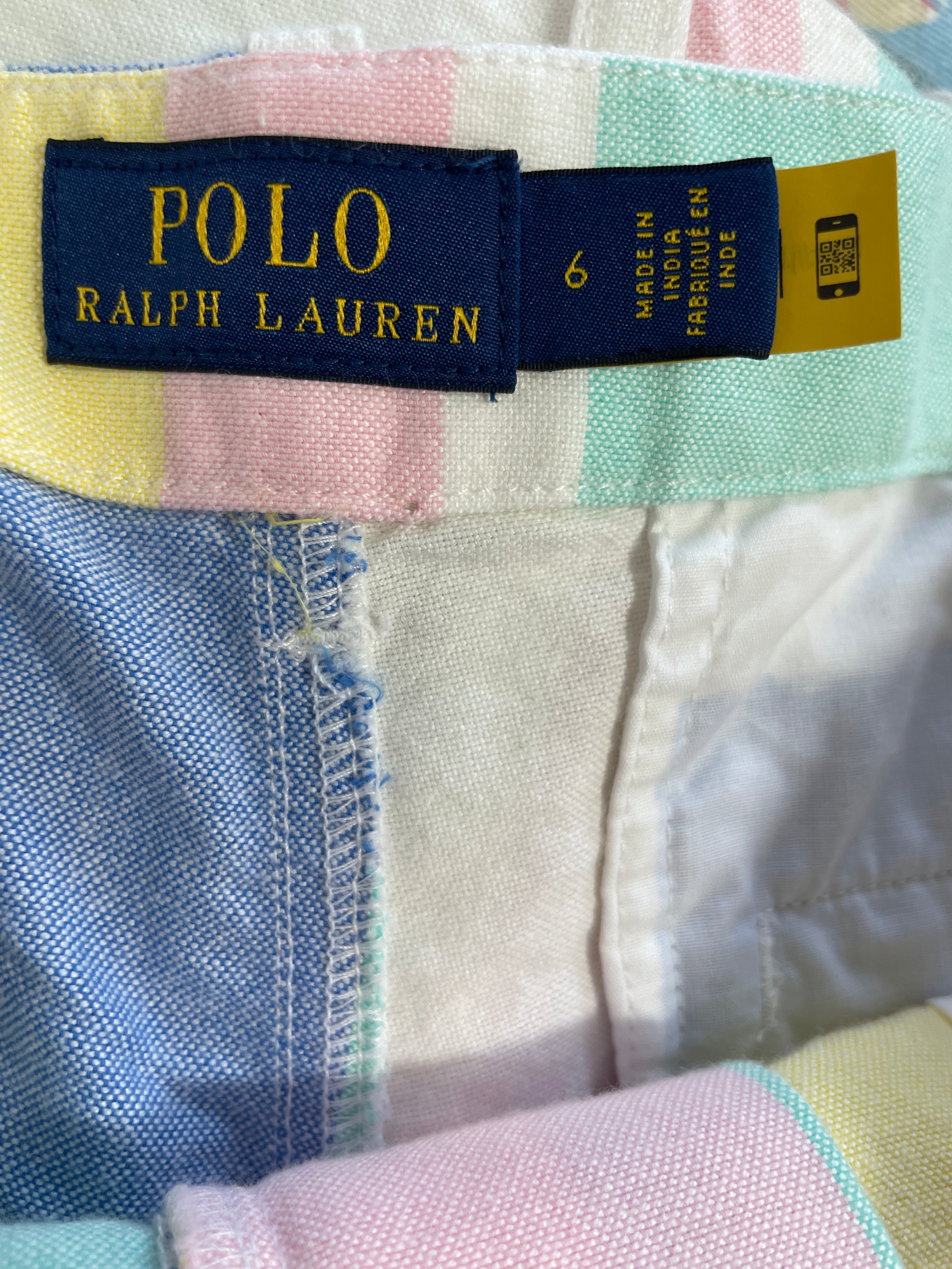 Close-up of a Polo Ralph Lauren garment waistband showing the navy brand label with gold lettering, size 6, and a yellow care tag, over pastel multicolor striped fabric.