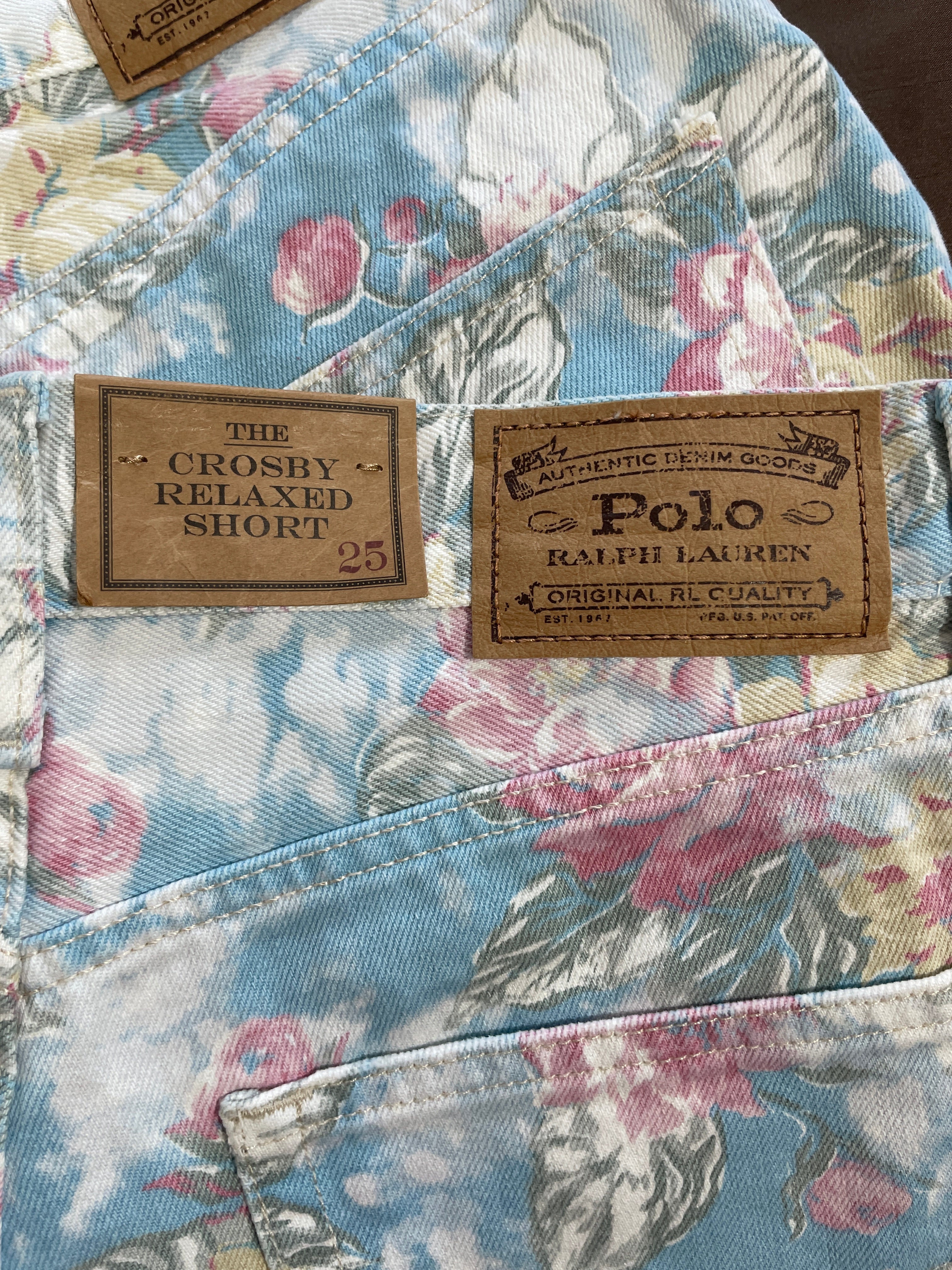 Close-up of the back waistband and pocket of a Ralph Lauren Polo short, showing a floral print in light blue, pink, and white, with two brown brand patches visible.
