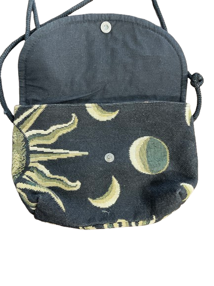 A small woven crossbody bag with a dark charcoal gray body and a front pocket featuring a celestial tapestry pattern of a sun and moon phases in beige, olive green, and gray.