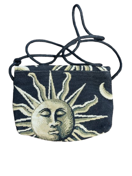 A small woven crossbody bag featuring a celestial tapestry design with a sun face, moon, and rays in beige and cream on a dark navy background, complete with a matching dark woven strap.