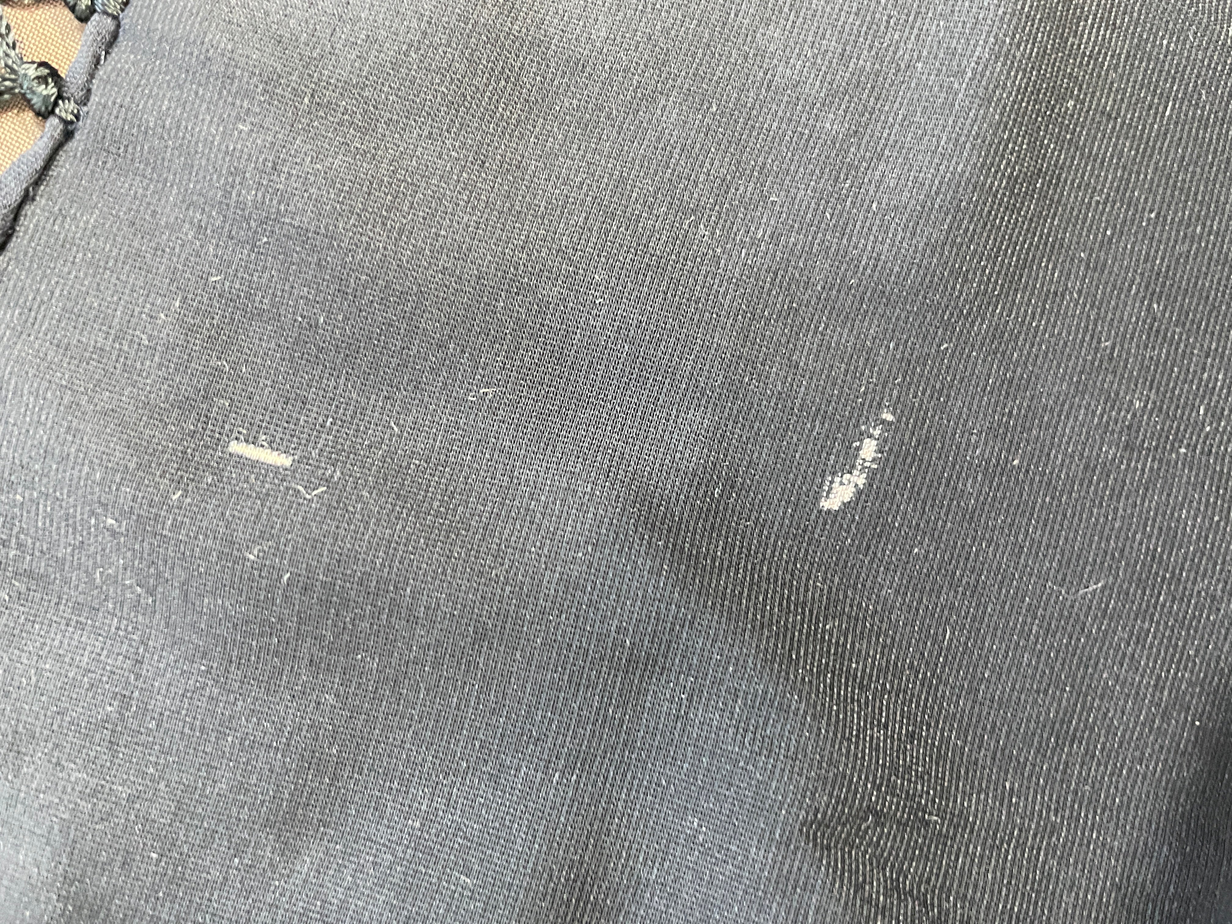 Close-up of dark gray woven fabric with visible lint, dust, and small white scratch marks on the surface.