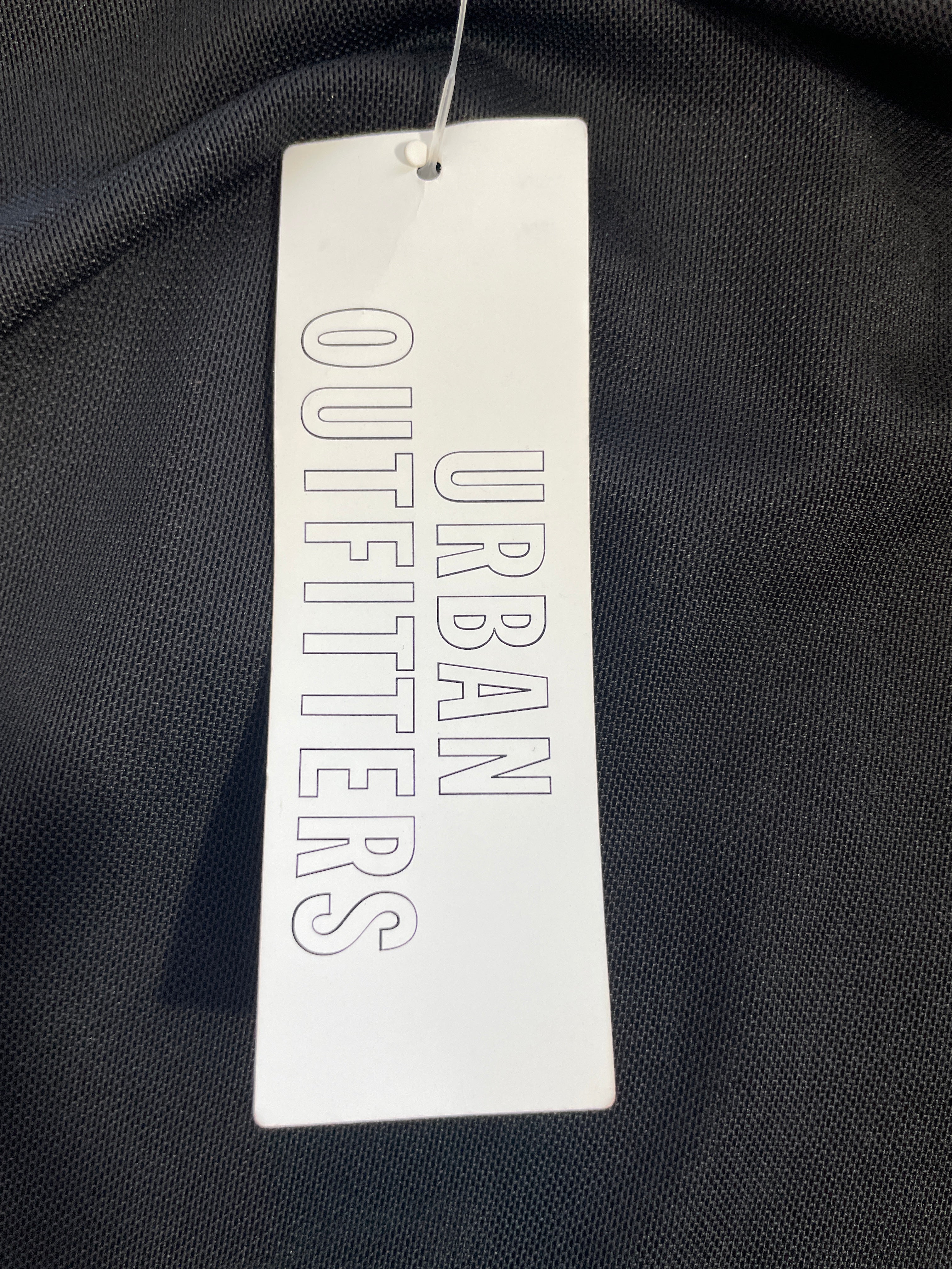 A white rectangular hangtag with the text 'Urbain Outfitters' printed vertically in gray, attached to a black textured garment.