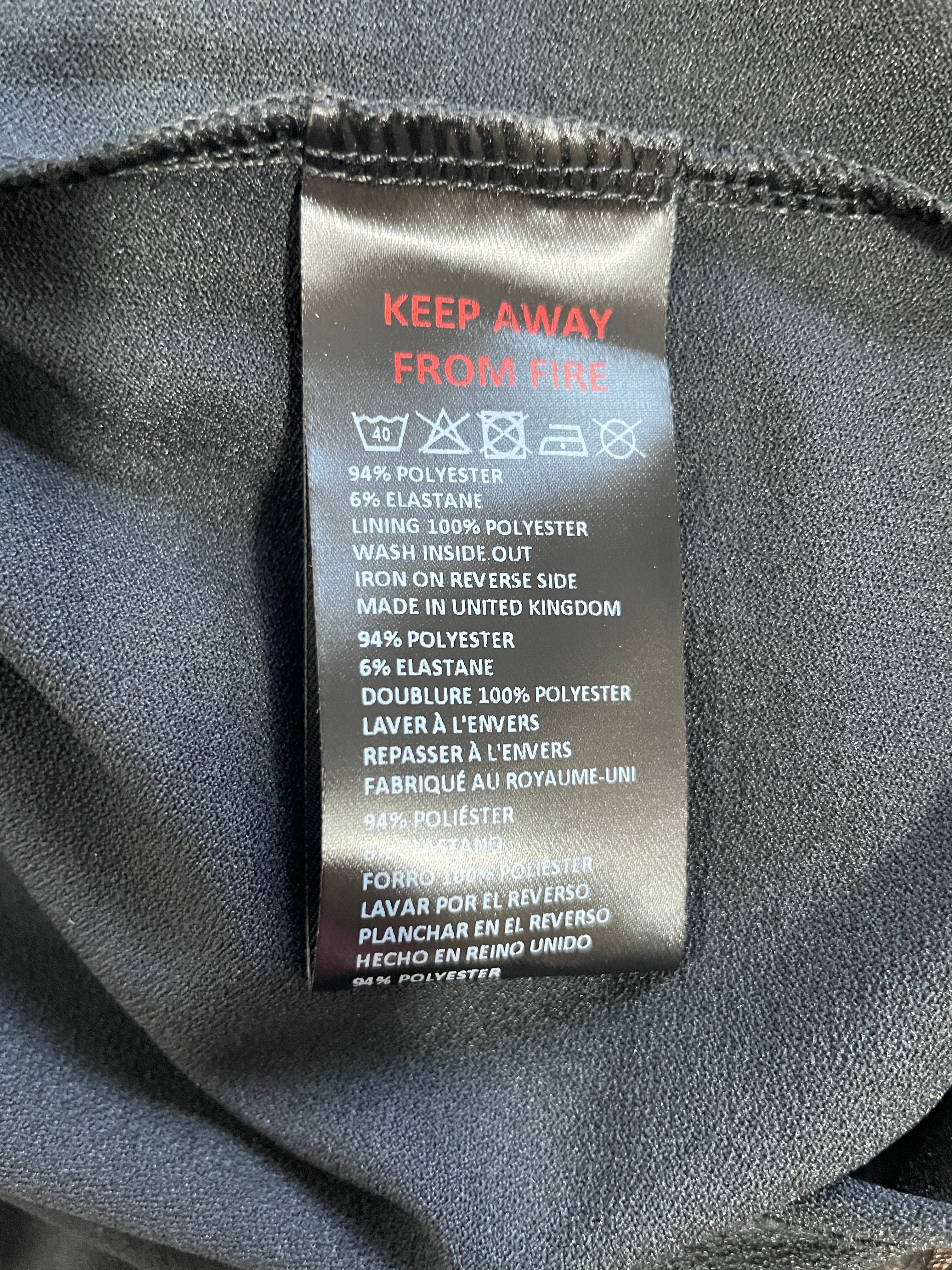 Close-up of a garment's interior neck label reading 'KEEP AWAY FROM FIRE' with care symbols and fabric composition details, set against dark gray fabric.