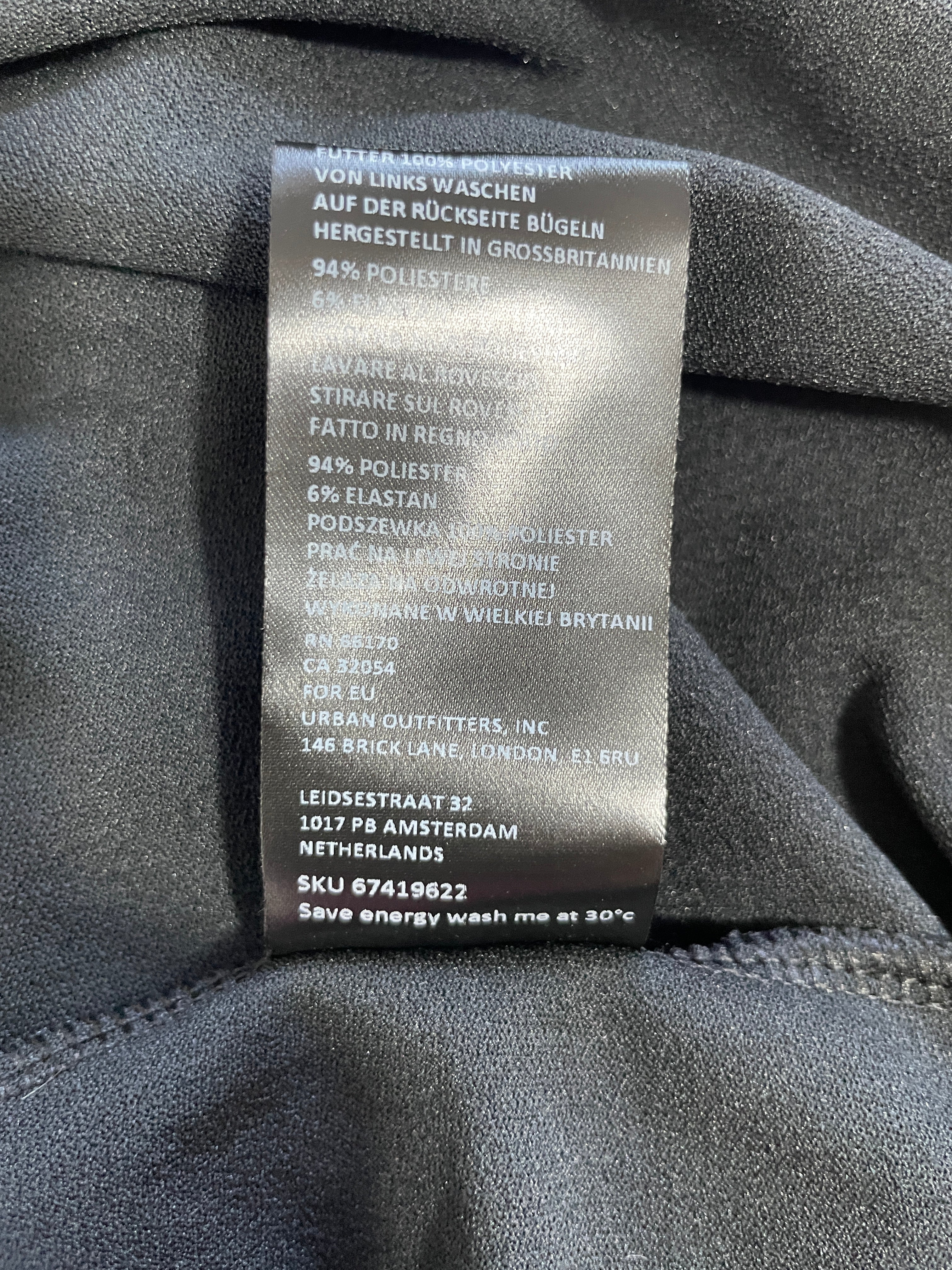 A close-up of a garment's interior label showing details like material composition (94% polyester, 6% elastan) and manufacturer information for Urban Outfitters, Inc.
