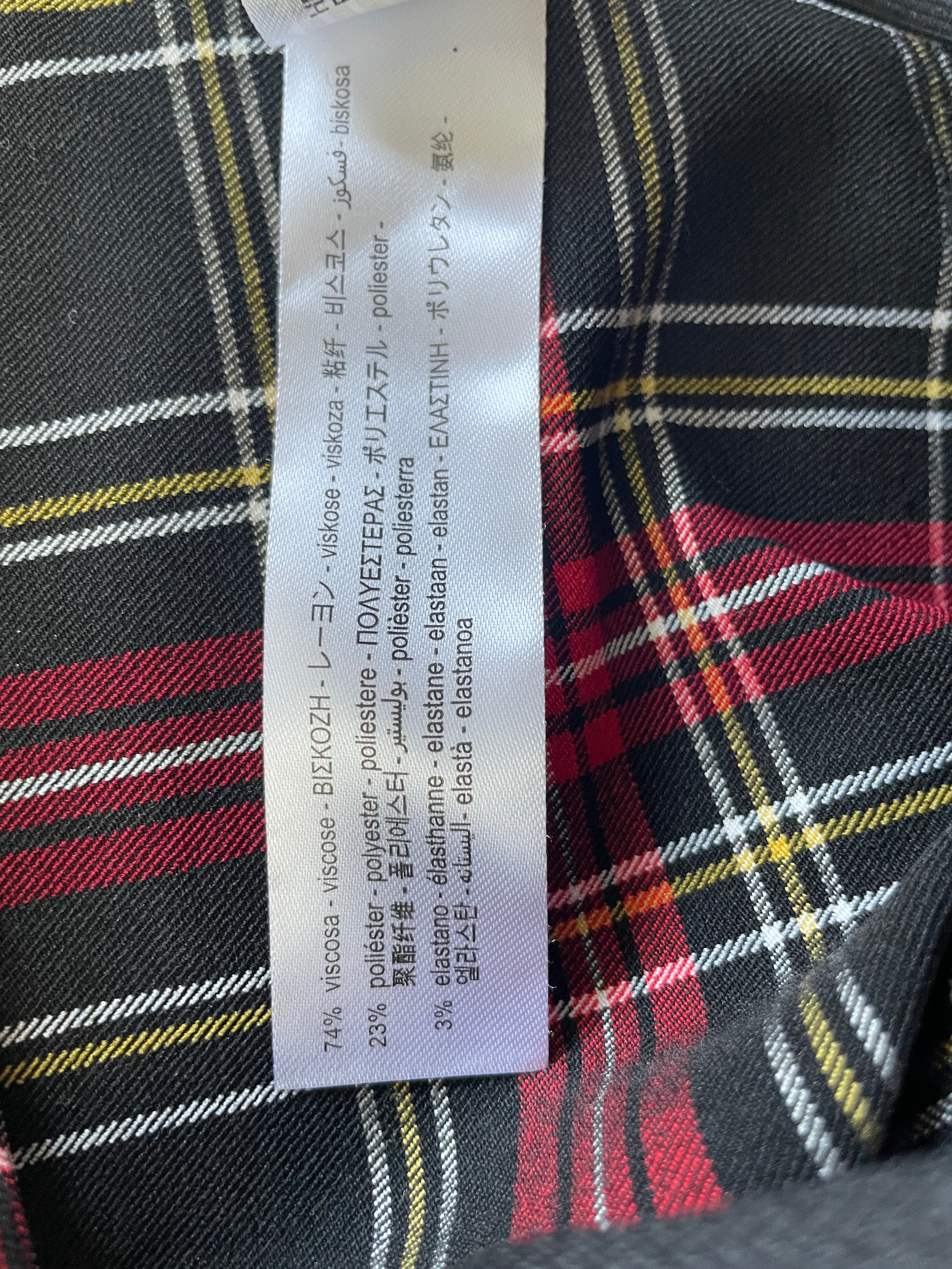 A close-up of a garment's interior label sewn onto a black, red, and yellow plaid fabric. The label contains multilingual text detailing the composition and properties of the viscose and polyester blend.