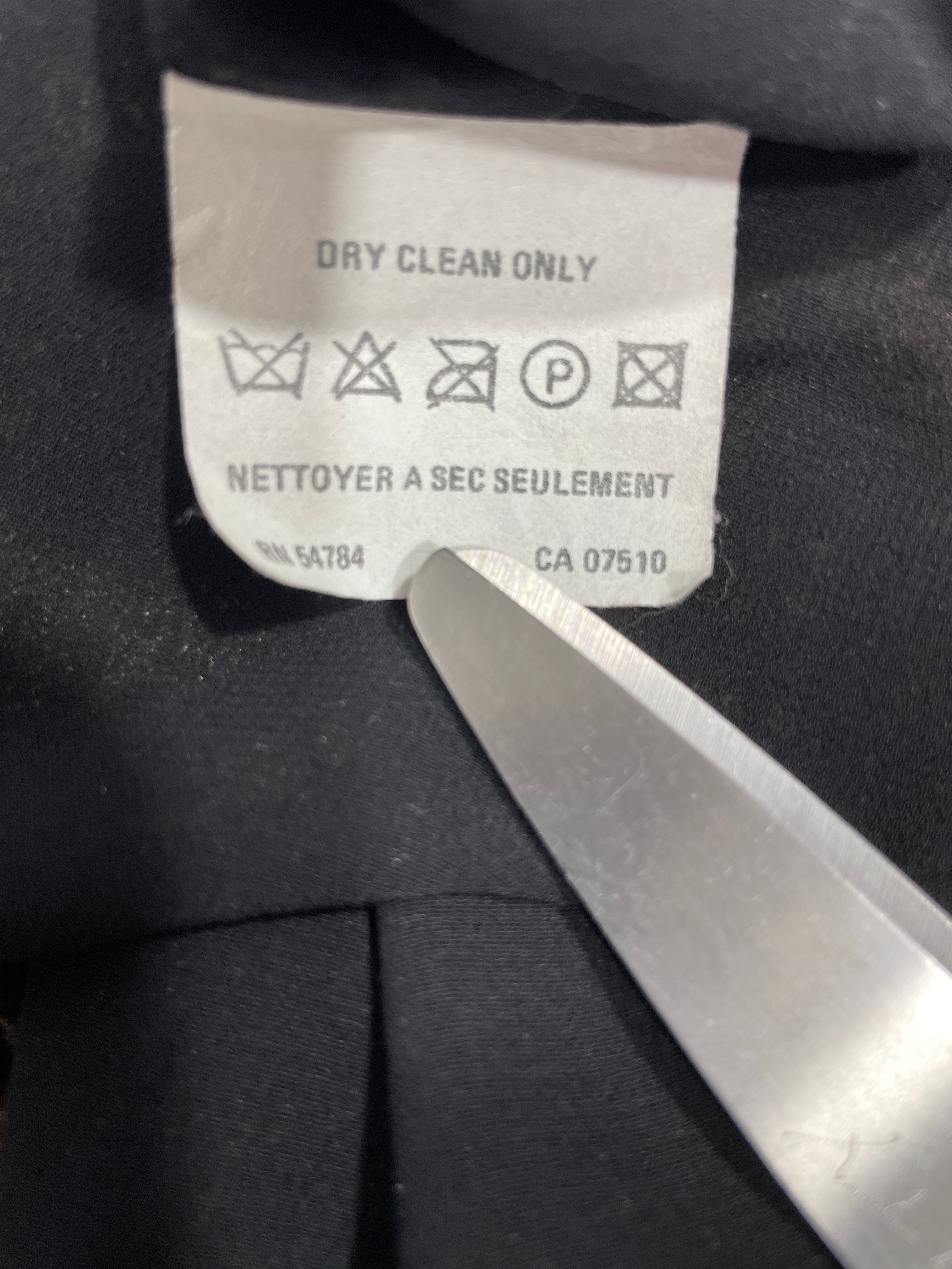 Close-up of a garment's interior neck label reading 'DRY CLEAN ONLY' with care symbols, held by a metal tool against black fabric.