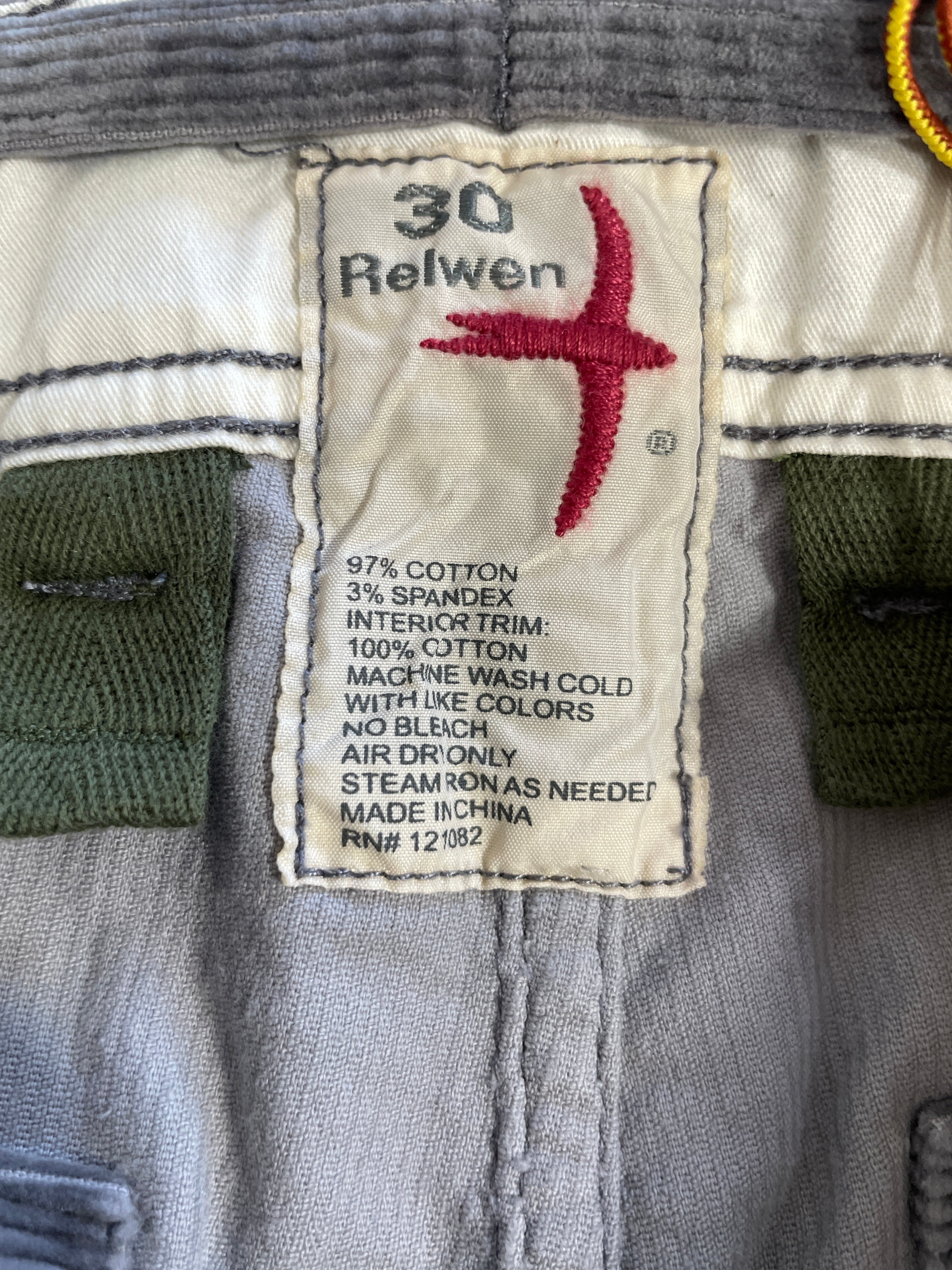 Close-up of a vintage pair of Relwen trousers showing the inner waistband and size label. The light gray denim fabric features green patch pockets and a cream-colored size 30 label with a red embroidered cross logo.