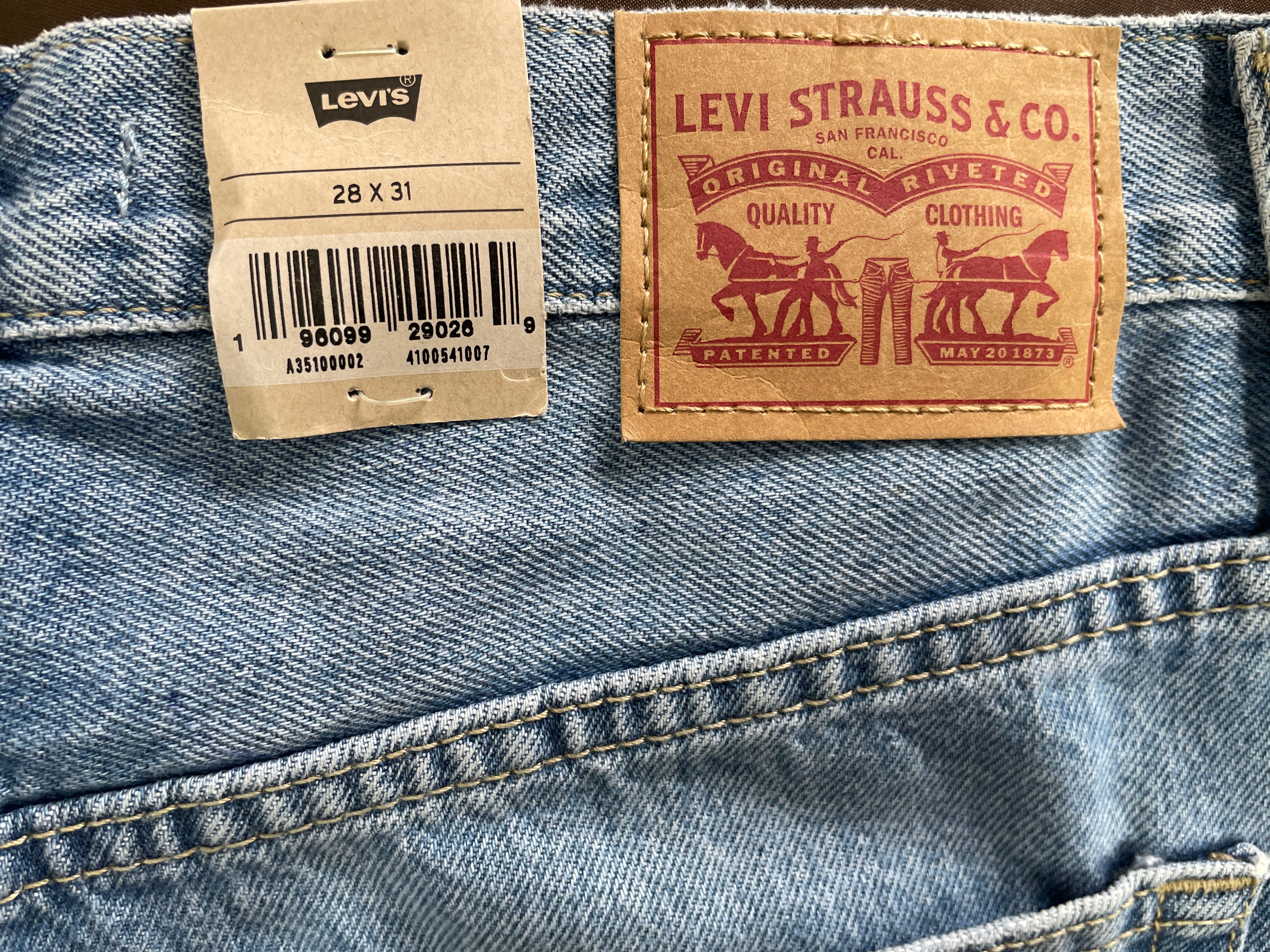 Close-up of the back waistband of a pair of Levi's 28 x 31 size 14 blue jeans, showing the original paper tag on the left and the classic brown leather brand patch on the right.