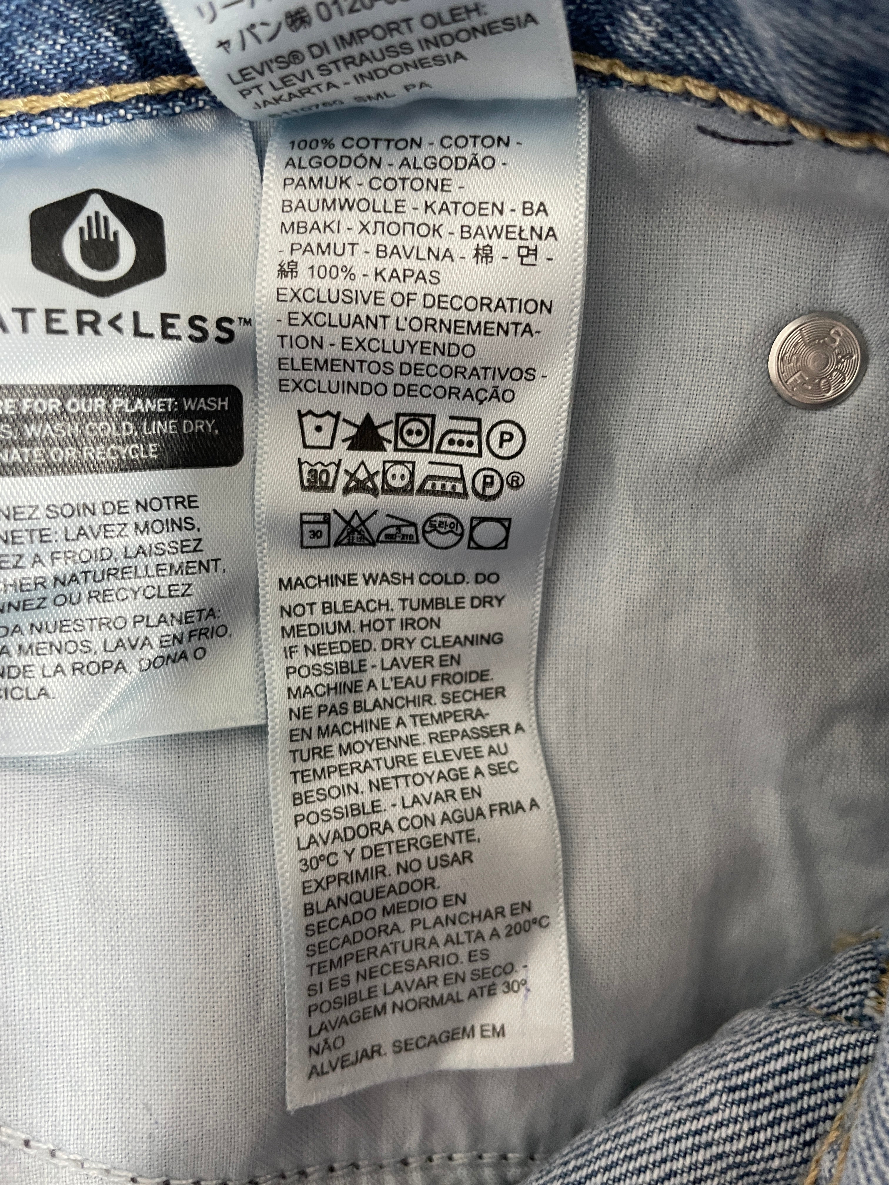 Close-up of a garment's inner care label with text in English and Spanish, care symbols, a small circular logo, and blue denim fabric visible around it.