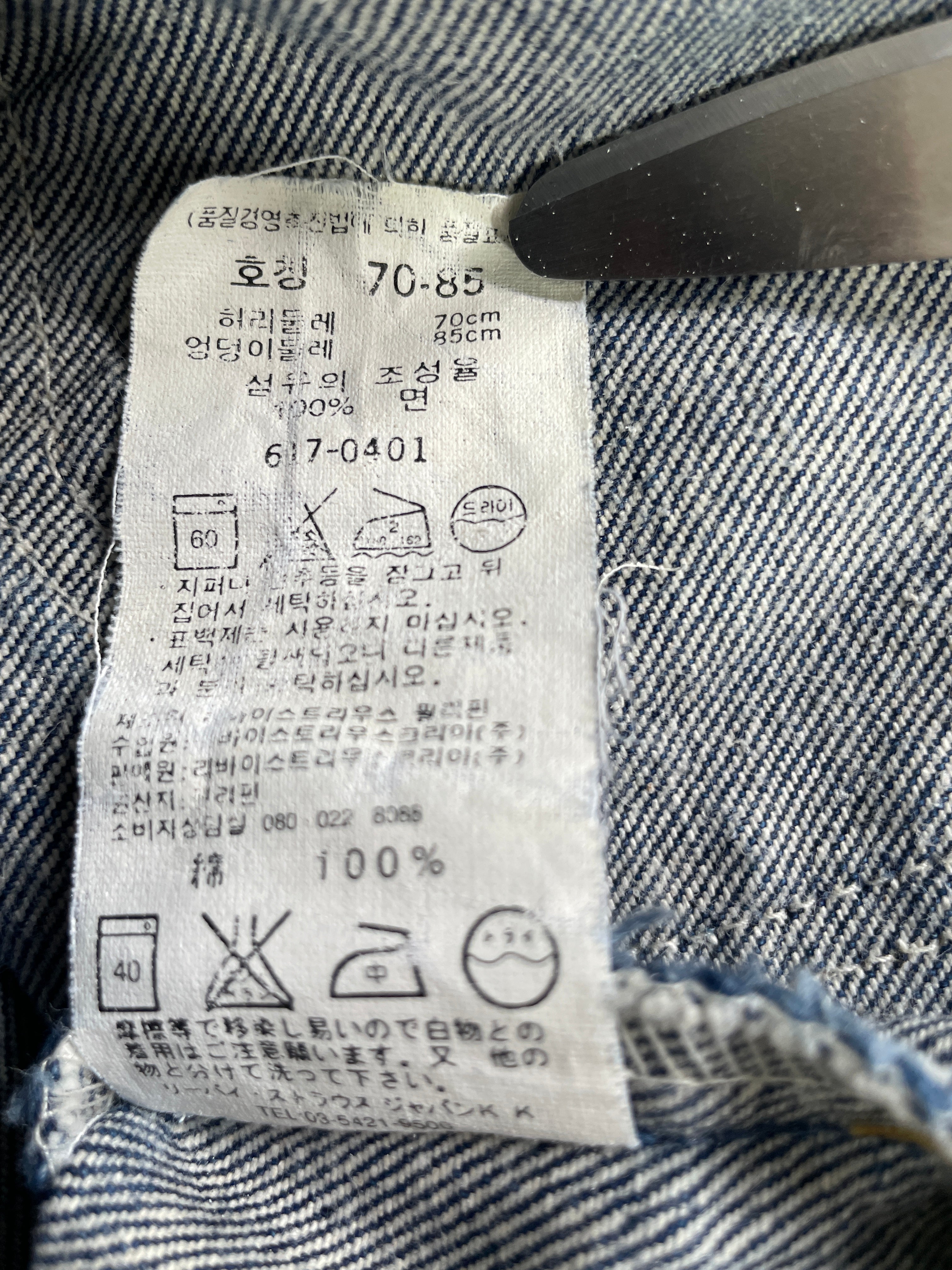Close-up of a white garment care label sewn onto blue denim fabric, with Korean text and laundry care symbols visible.