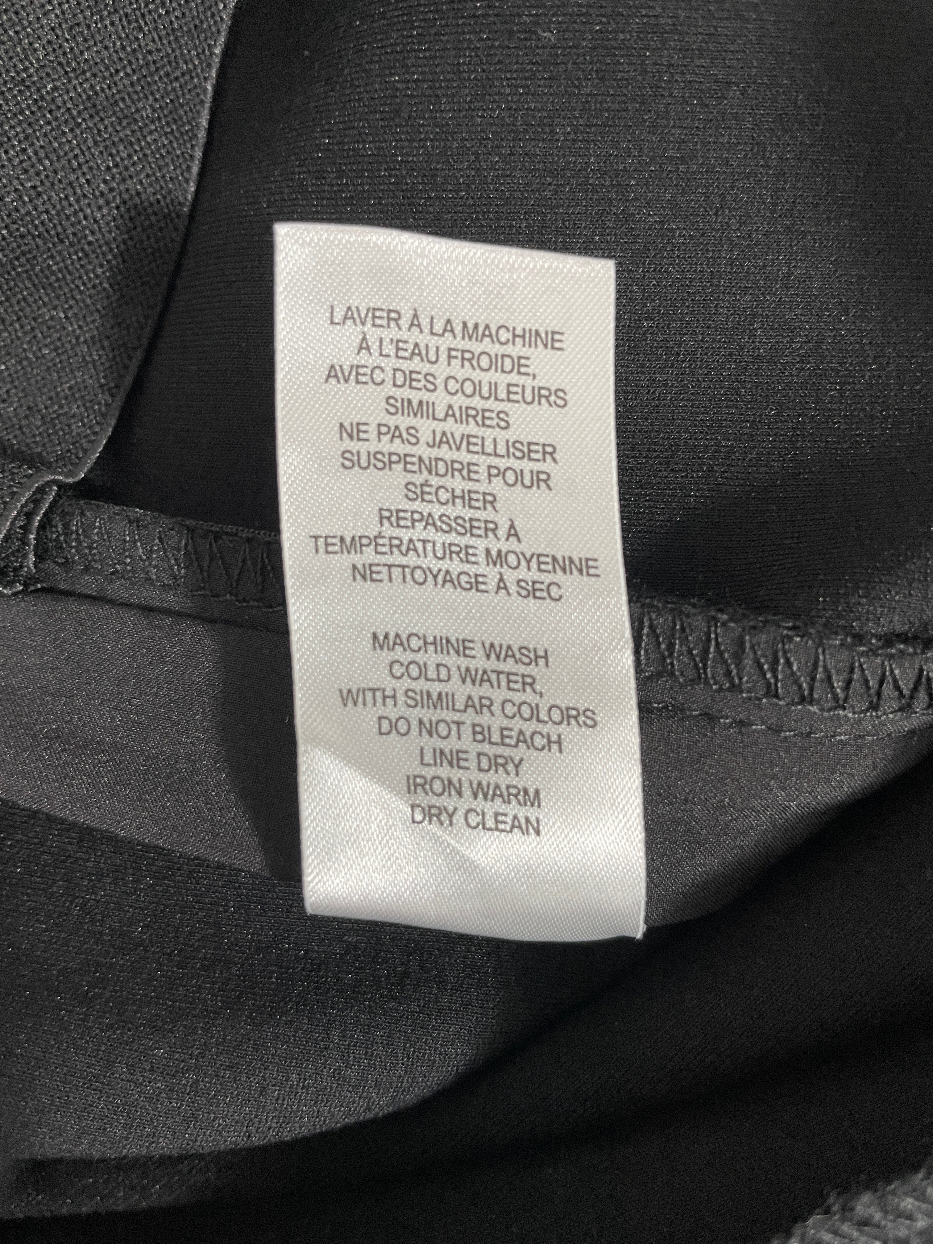 A close-up of a white garment care label sewn onto black fabric, showing French and English instructions for machine washing and drying.