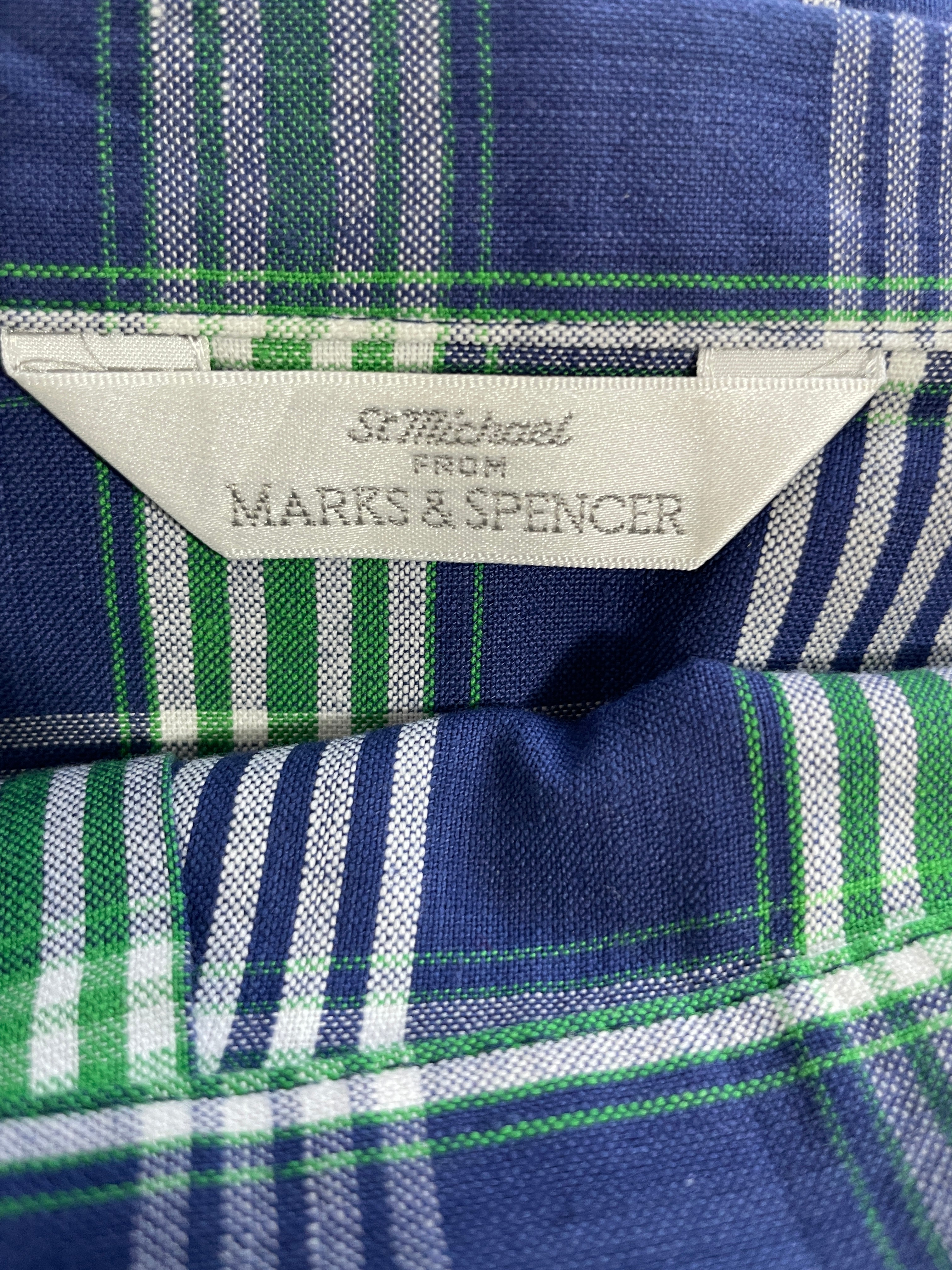 Close-up of a plaid shirt fabric in navy blue, green, and white, showing a sewn-in label that reads 'St. Michael From Marks & Spencer'.