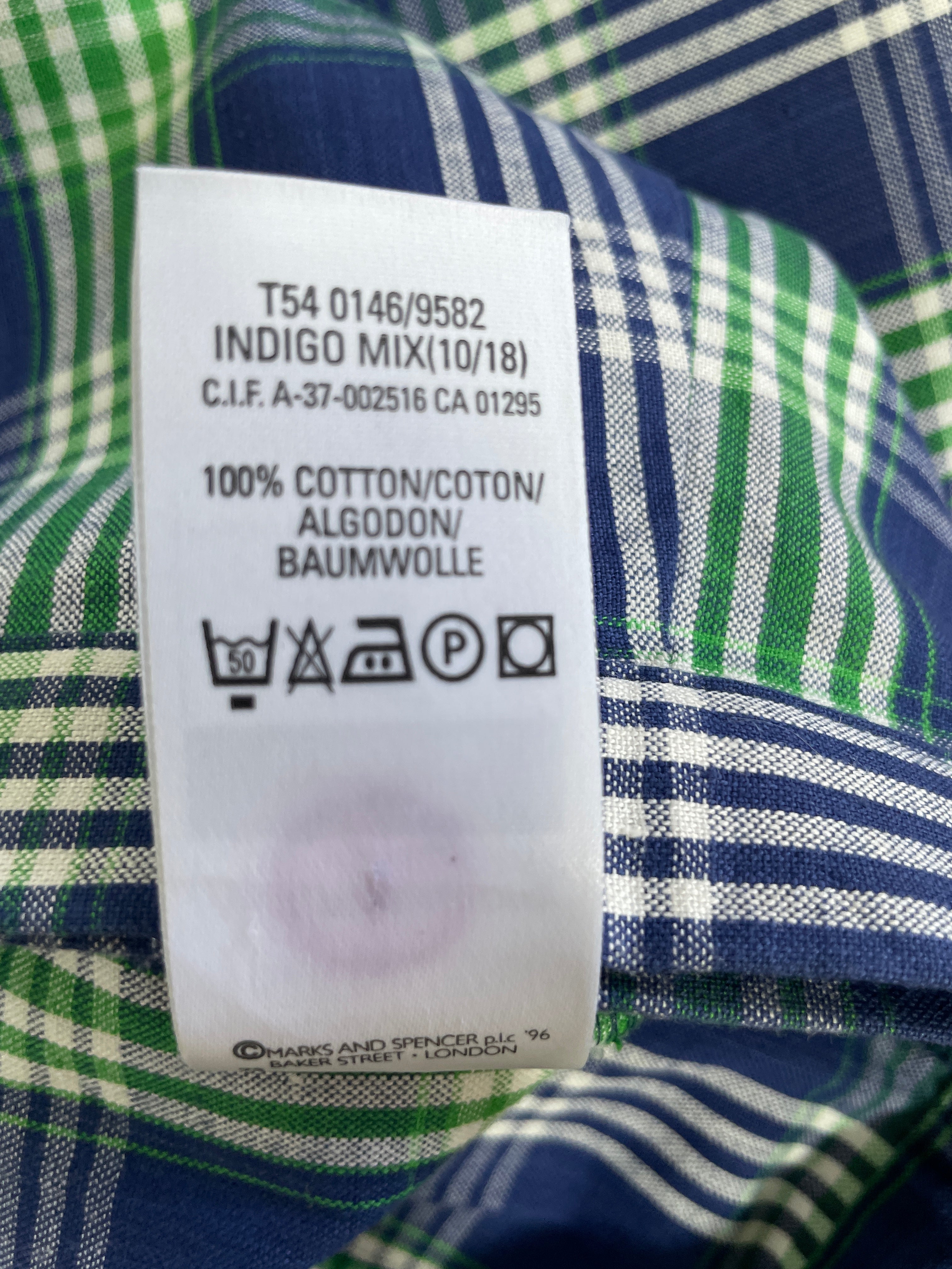 A close-up of a white garment care label sewn onto a green, white, and navy plaid fabric.