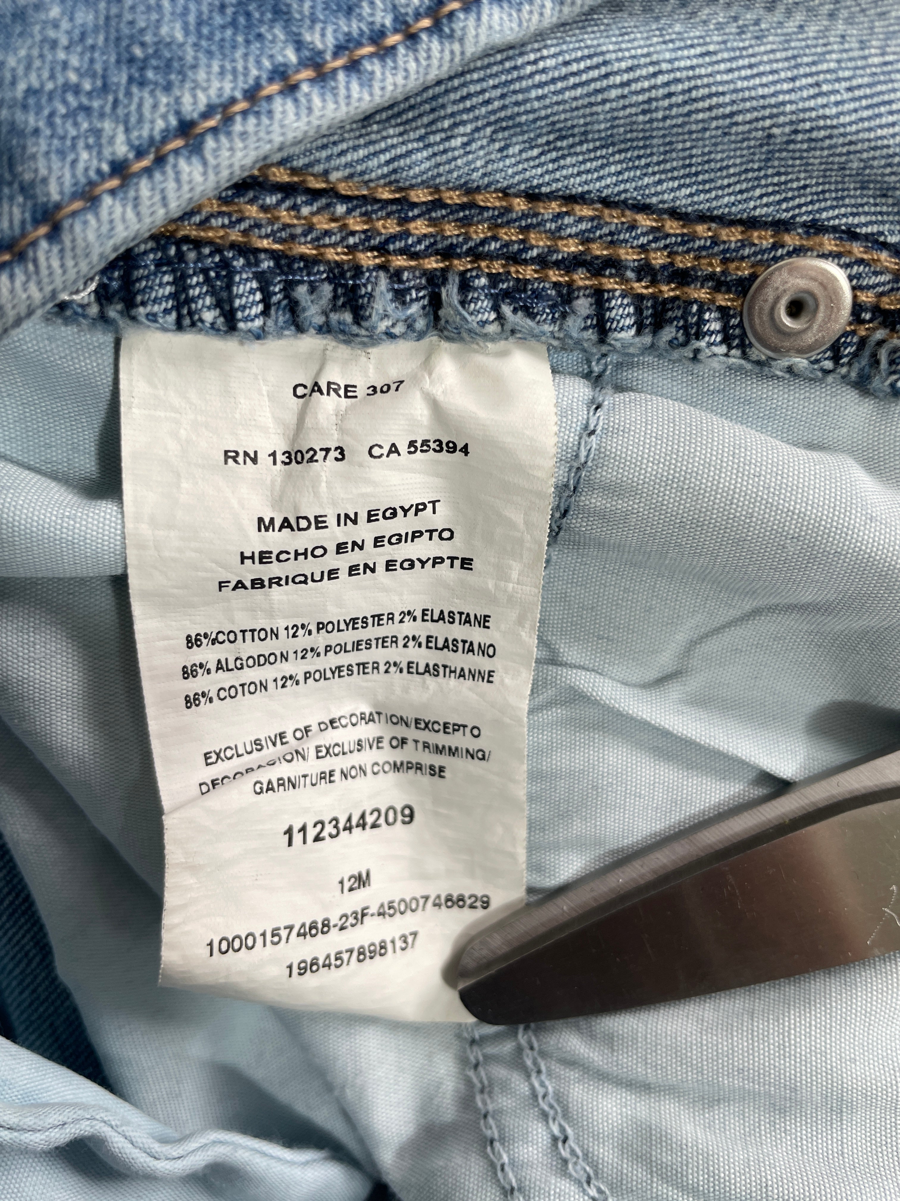 Close-up of a white garment care label sewn inside a pair of blue denim jeans, with the denim and metal button visible around it.