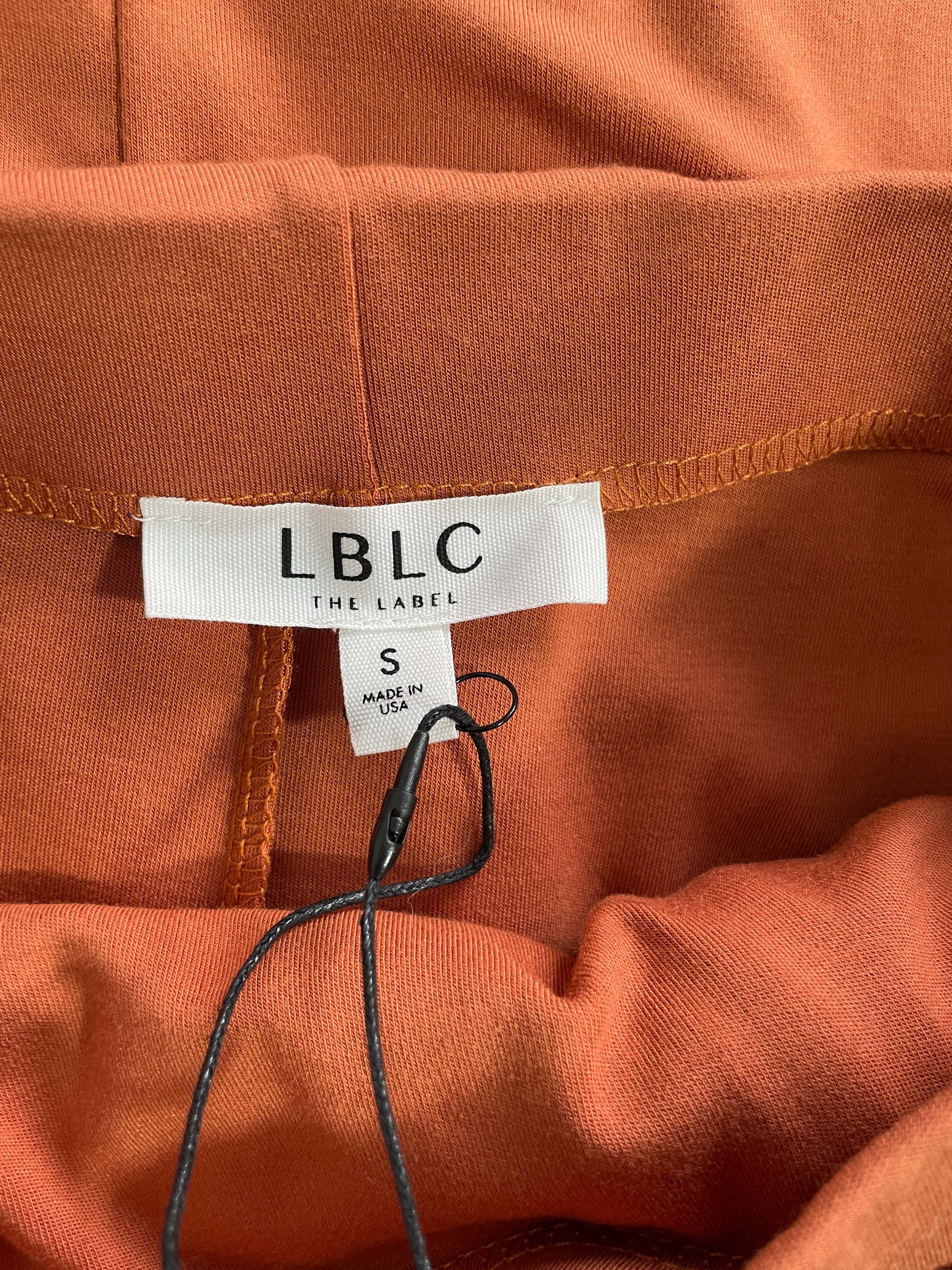 Close-up of the inner waistband of an orange-brown garment, showing a white LBLC THE LABEL brand tag and a size S label.