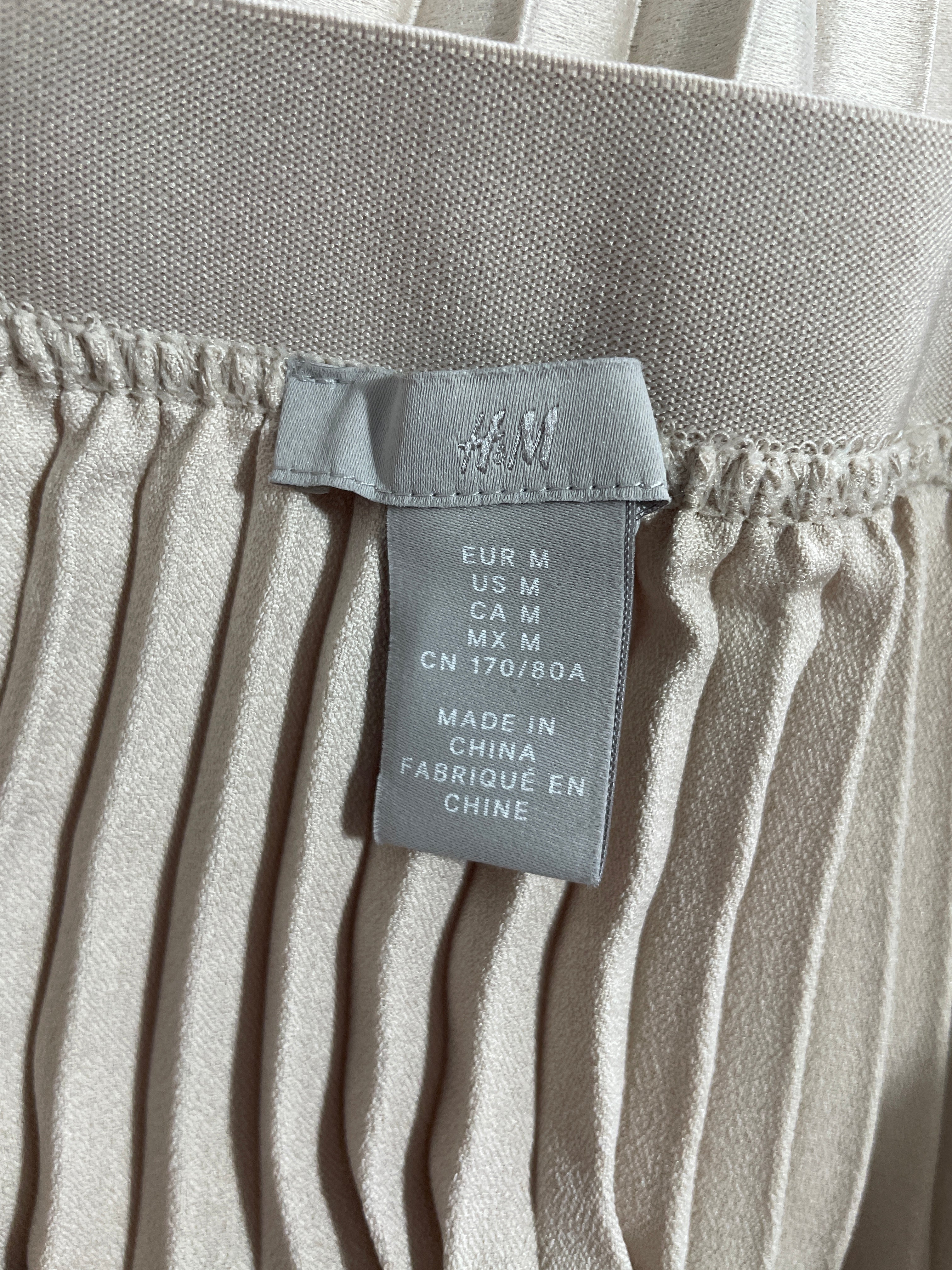 1. H&M size medium garment label and finely pleated beige skirt fabric