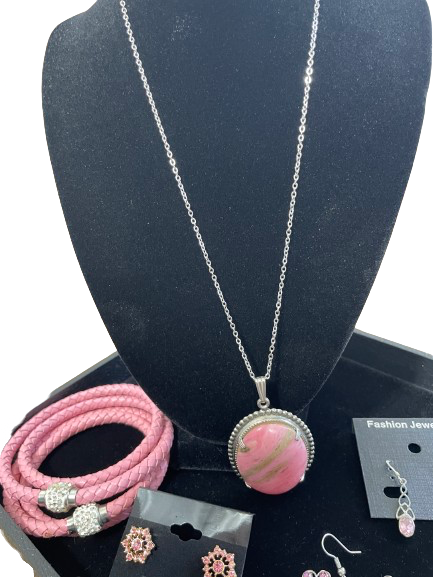 Necklace with pink stone pendant on a black mannequin bust, with pink bracelet and earrings displayed below.