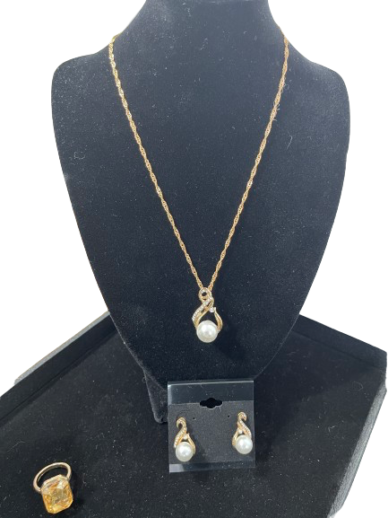 Jewelry set with gold necklace, earrings, and ring on a black stand.