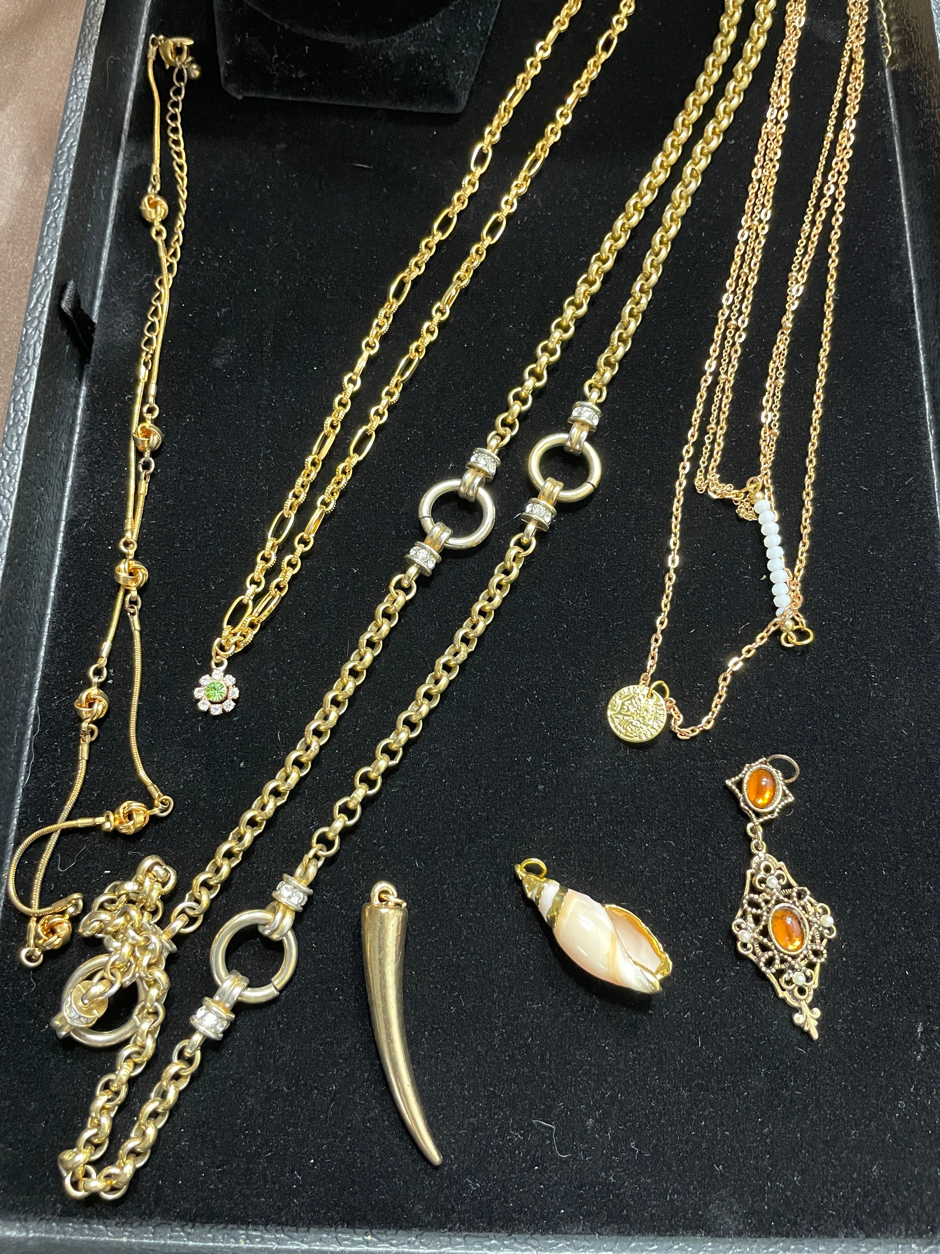 Close-up of five gold necklaces with pendants including shell and amber details