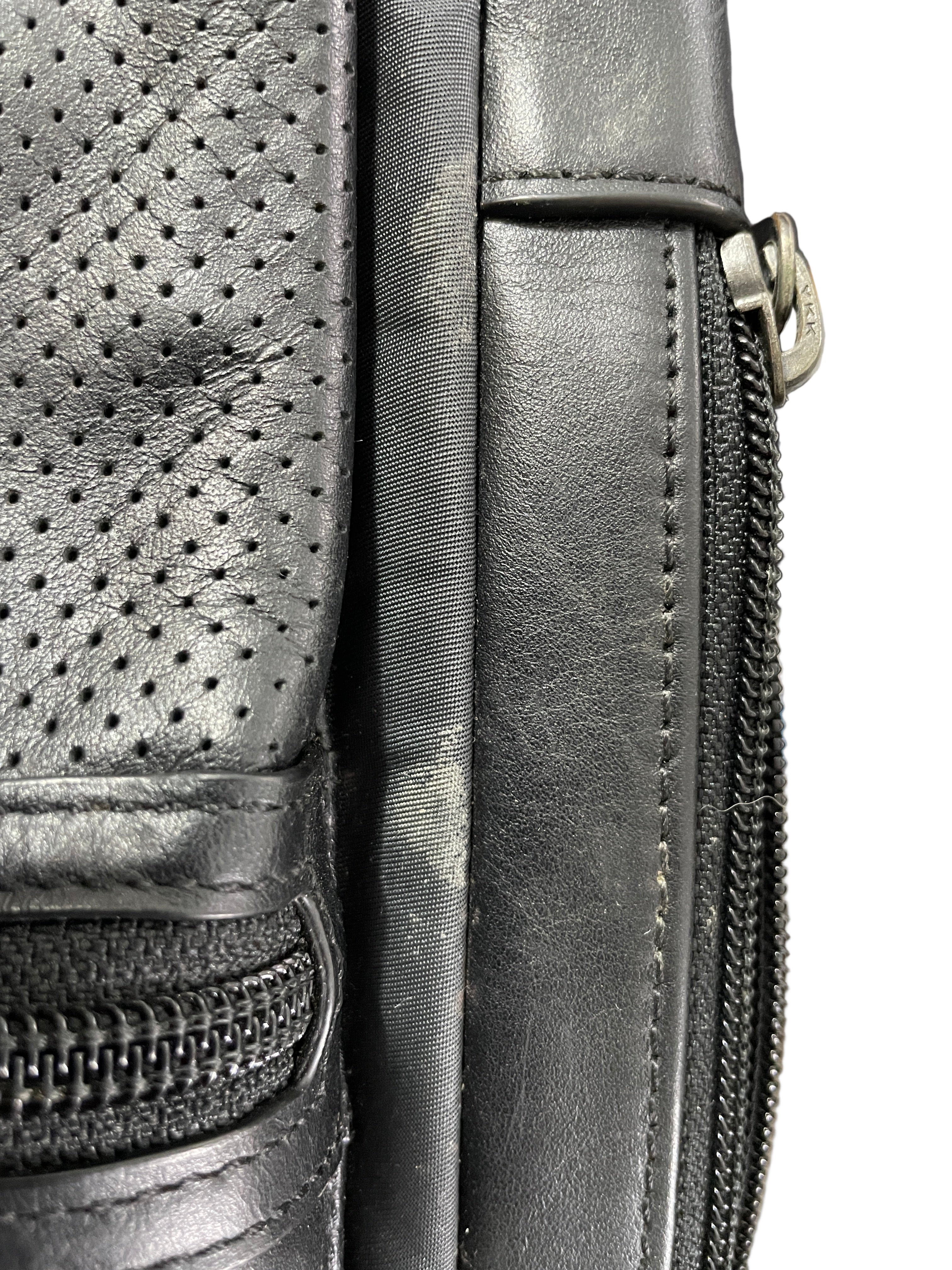 Close-up of a black leather bag with a zipper, showing signs of wear.