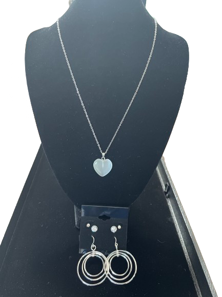 Silver necklace with heart pendant and earrings on a black stand.