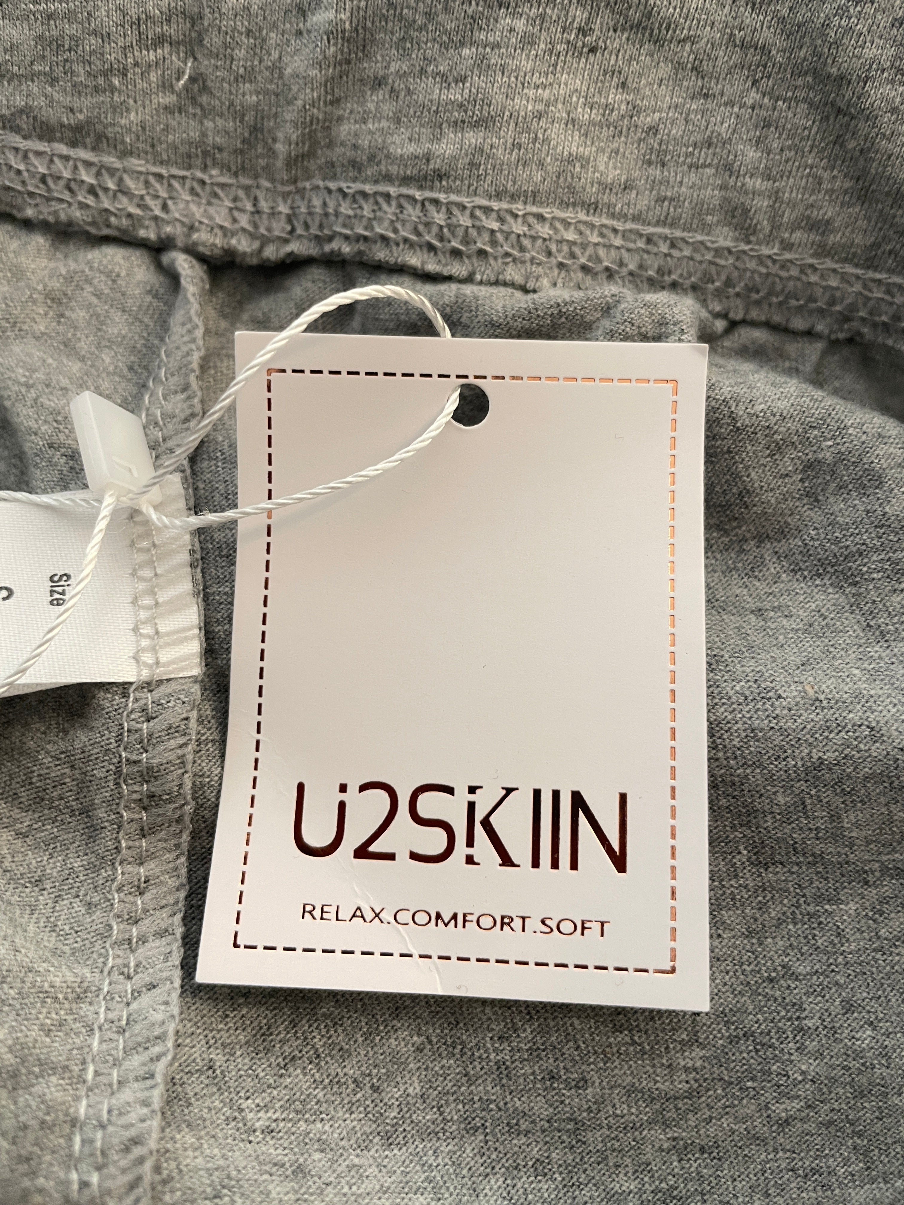 A close-up of gray heathered fabric with a white product tag attached by a white string. The tag is printed with the brand name 'U2SKIIN' and the text 'RELAX COMFORT SOFT'.