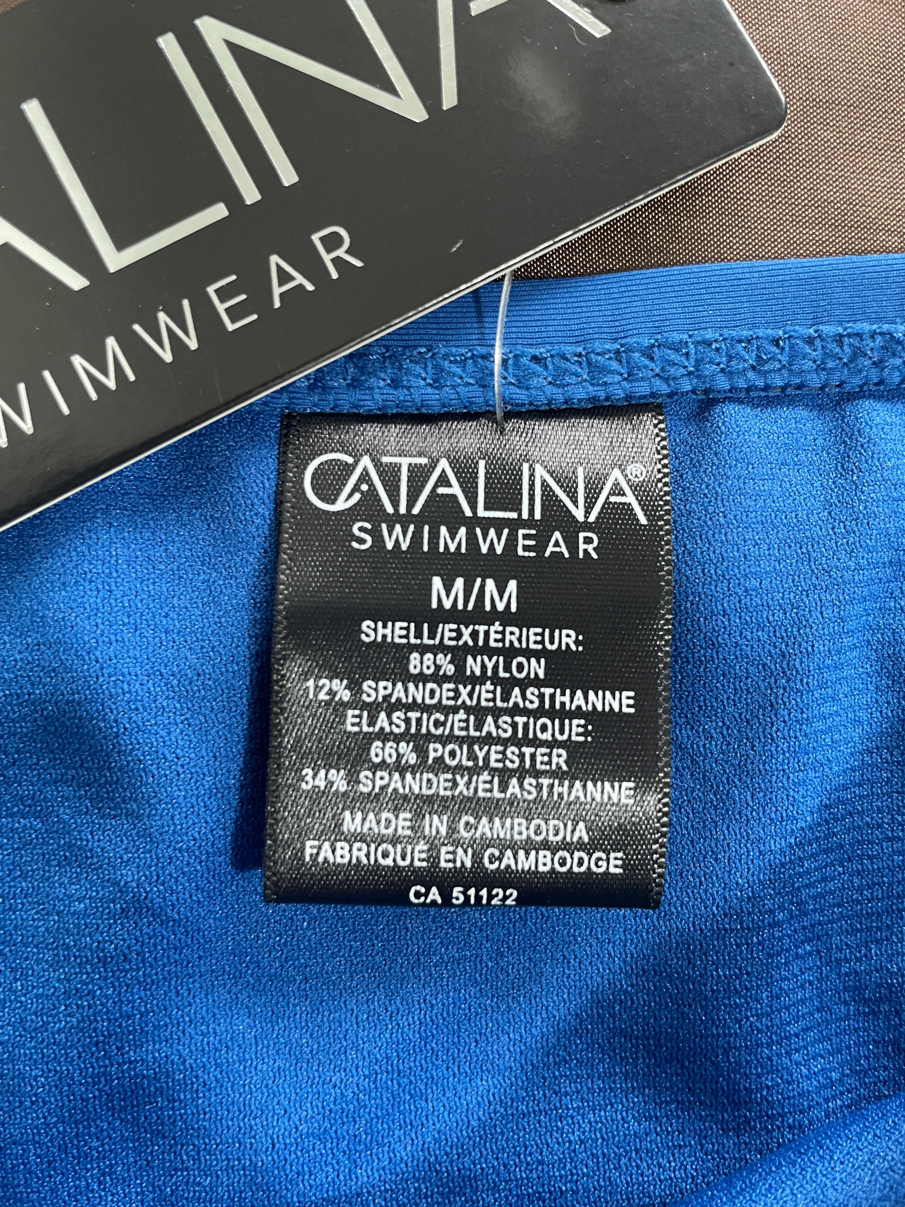 Close-up of a bright blue swimwear inner label reading CATALINA SWIMWEAR with size M/M details, next to a black hangtag.