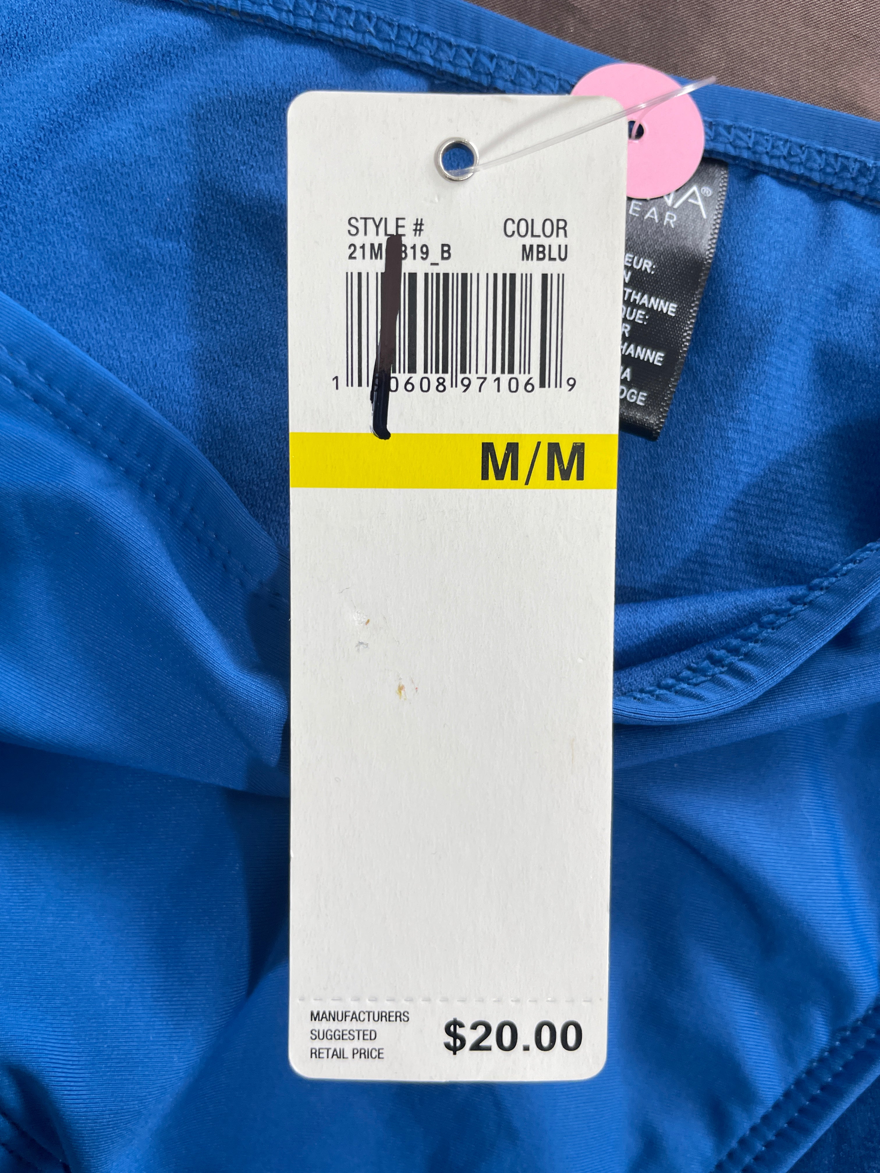 A close-up of a blue garment tag attached to a white size label, showing the text 'M/M' in a yellow band and a retail price of $20.00.