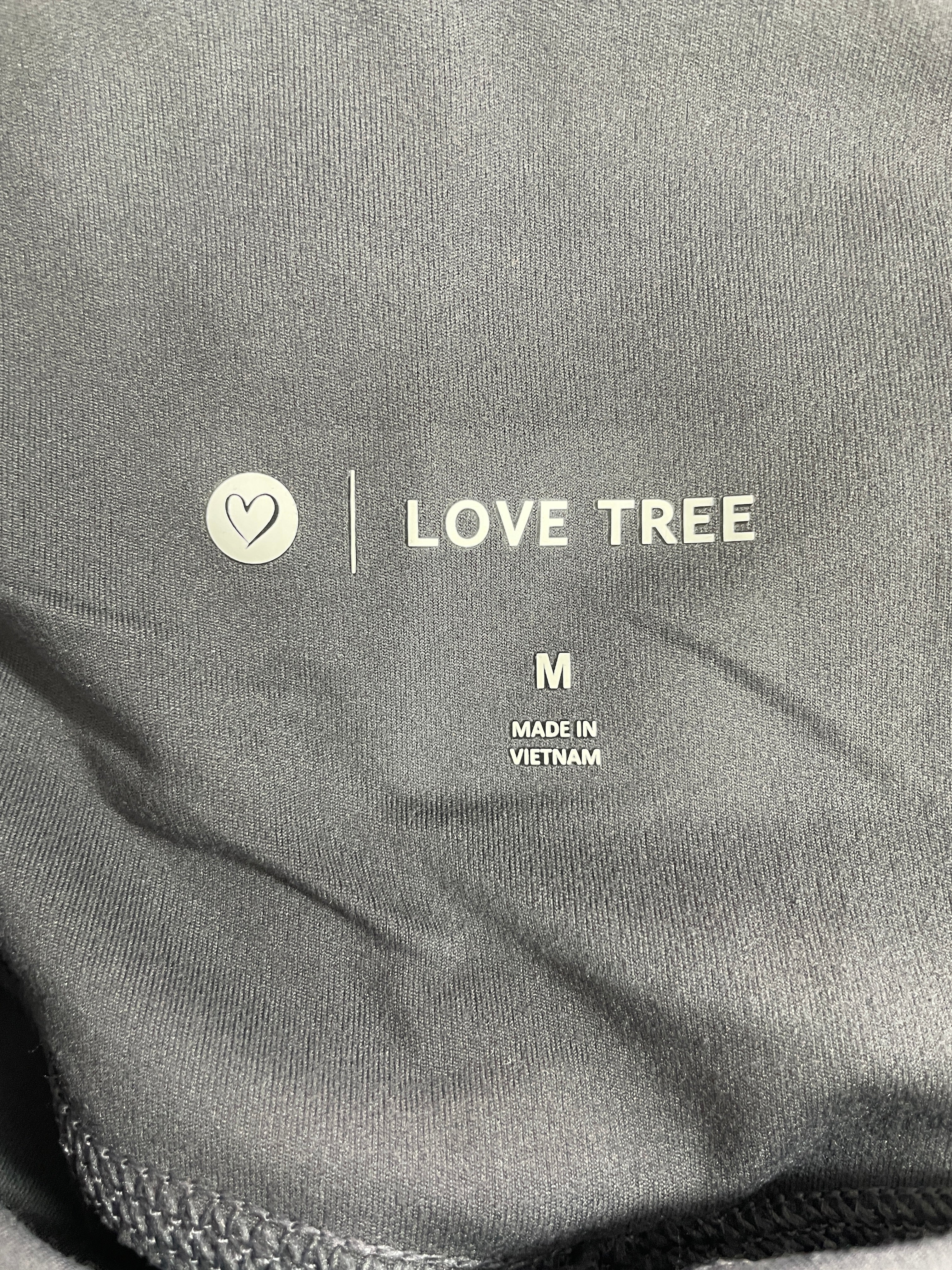 Close-up of a dark gray garment label reading LOVE TREE, with size M and MADE IN VIETNAM printed on the fabric.