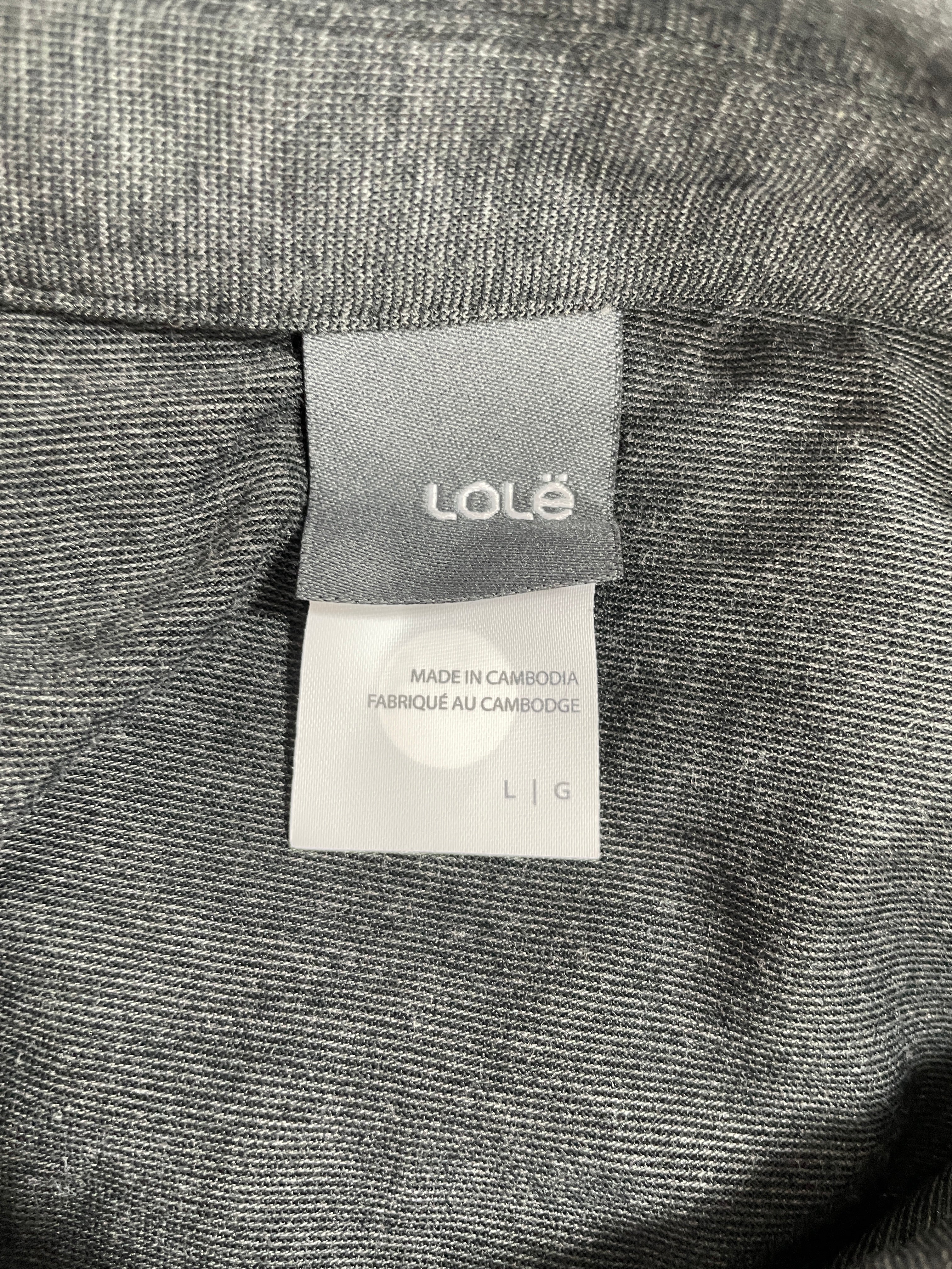 Close-up of a gray woven garment label reading LOLÉ, with a white tag below that says Made in Cambodia and size L|G, set against dark heather gray fabric.