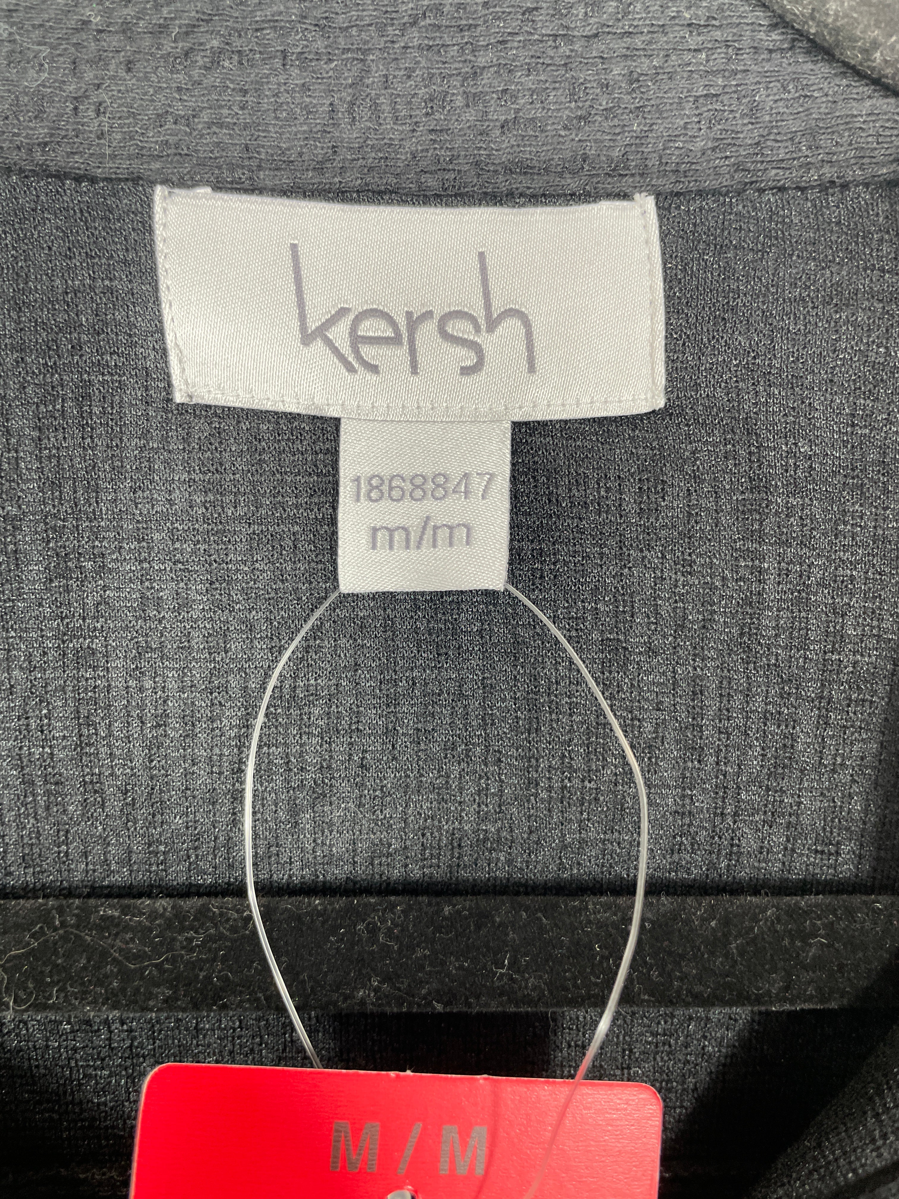 Close-up of a gray knit garment label reading 'kersh' with size information '1868847 m/m' and a red size tag below, set against the dark textured fabric.