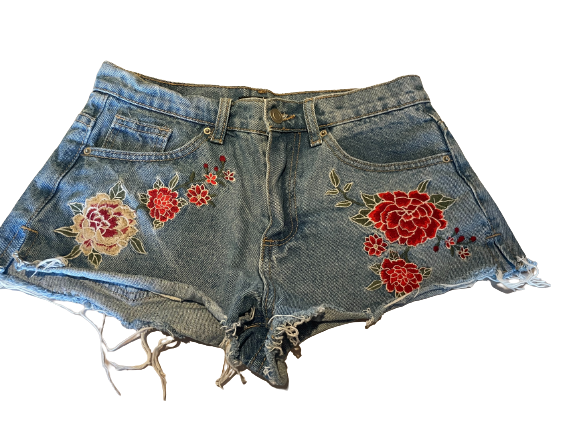 A pair of blue denim shorts with embroidered roses on the sides, featuring a frayed hem and five pockets.