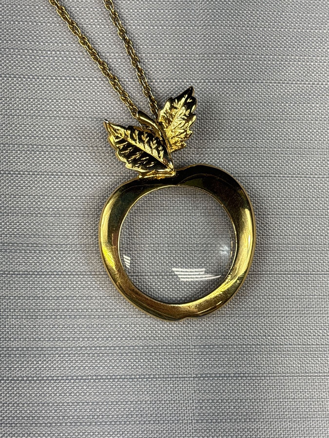 Close-up of apple magnifying glass pendant with gold tone leaves