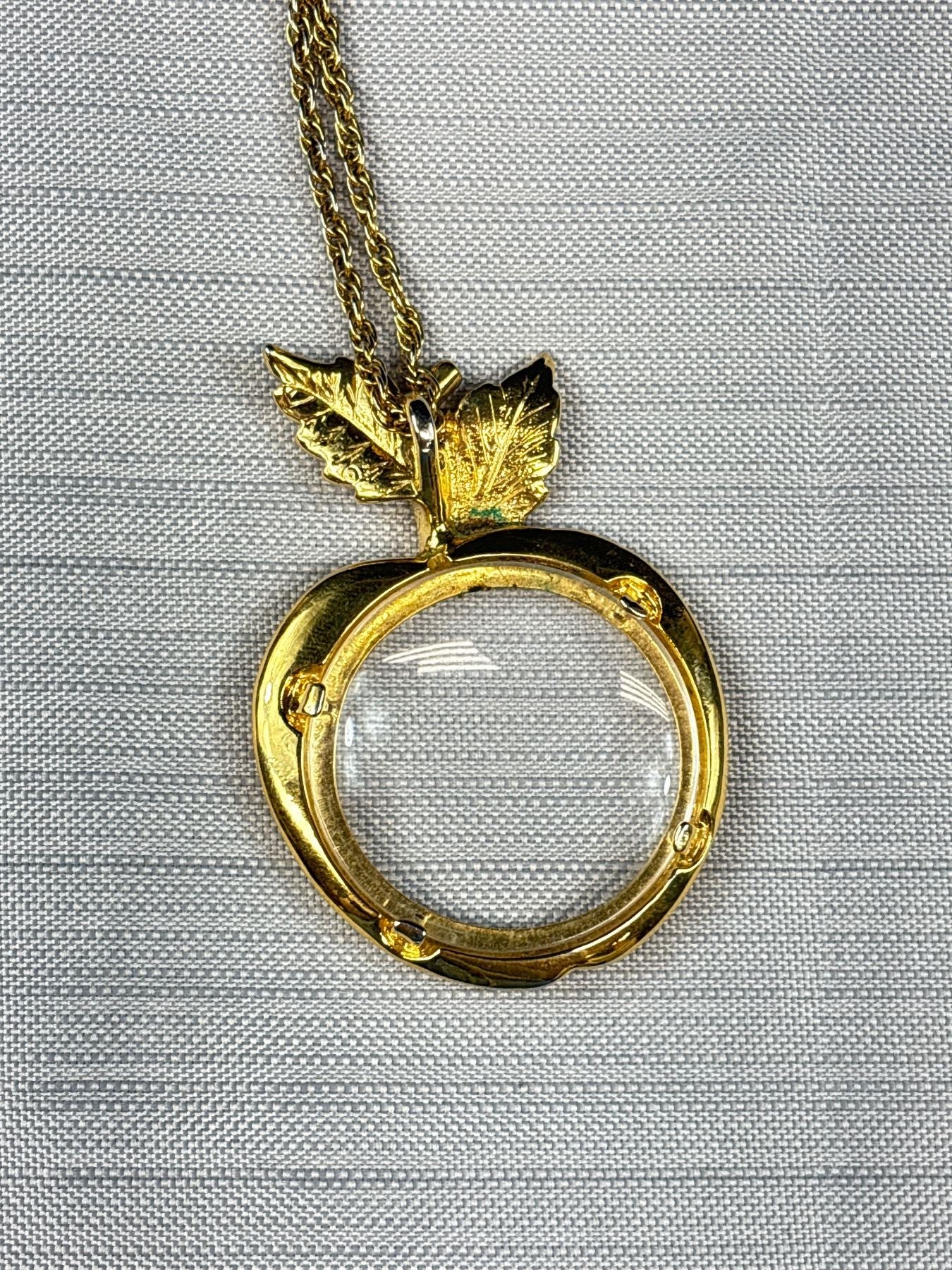 Close-up of apple magnifying glass pendant with gold tone leaves back view