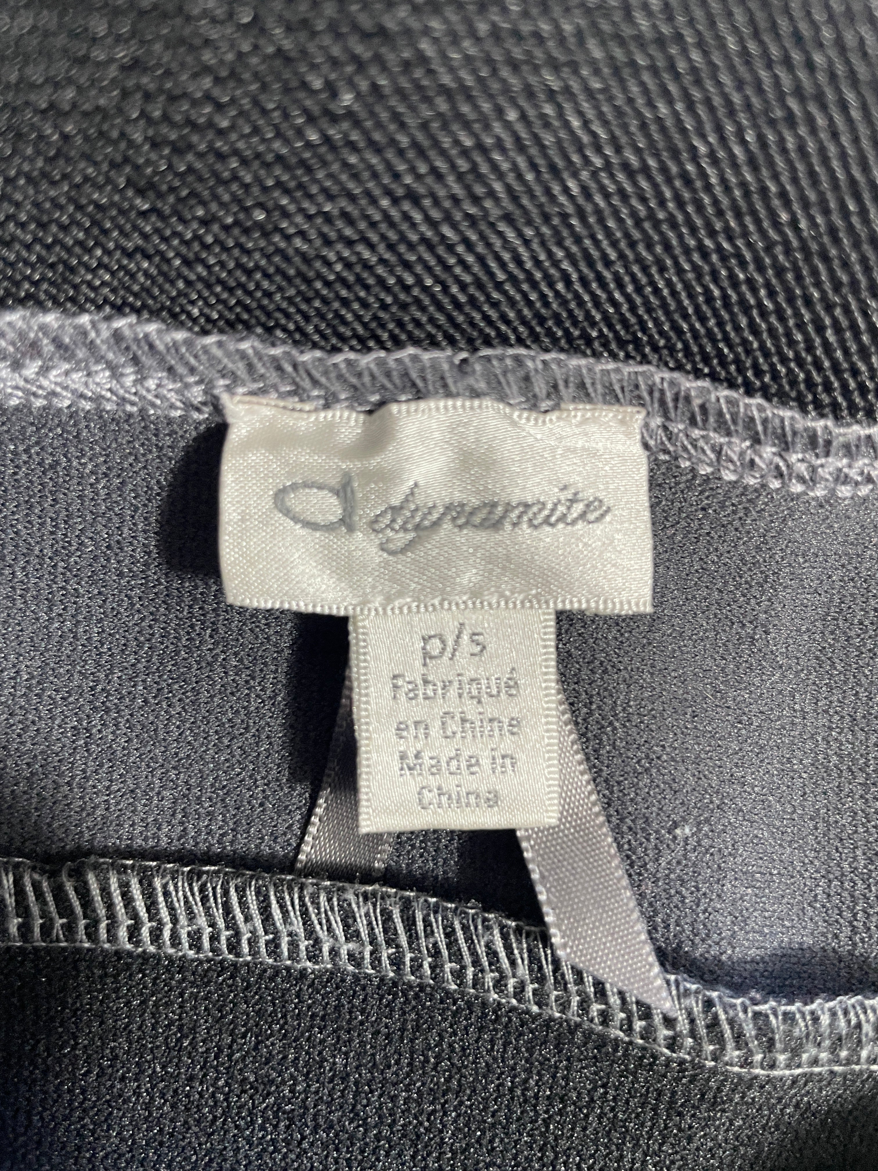 Close-up of a garment's interior label showing the brand 'Dynamite' on a white fabric tag, sewn onto dark gray textured knit fabric.