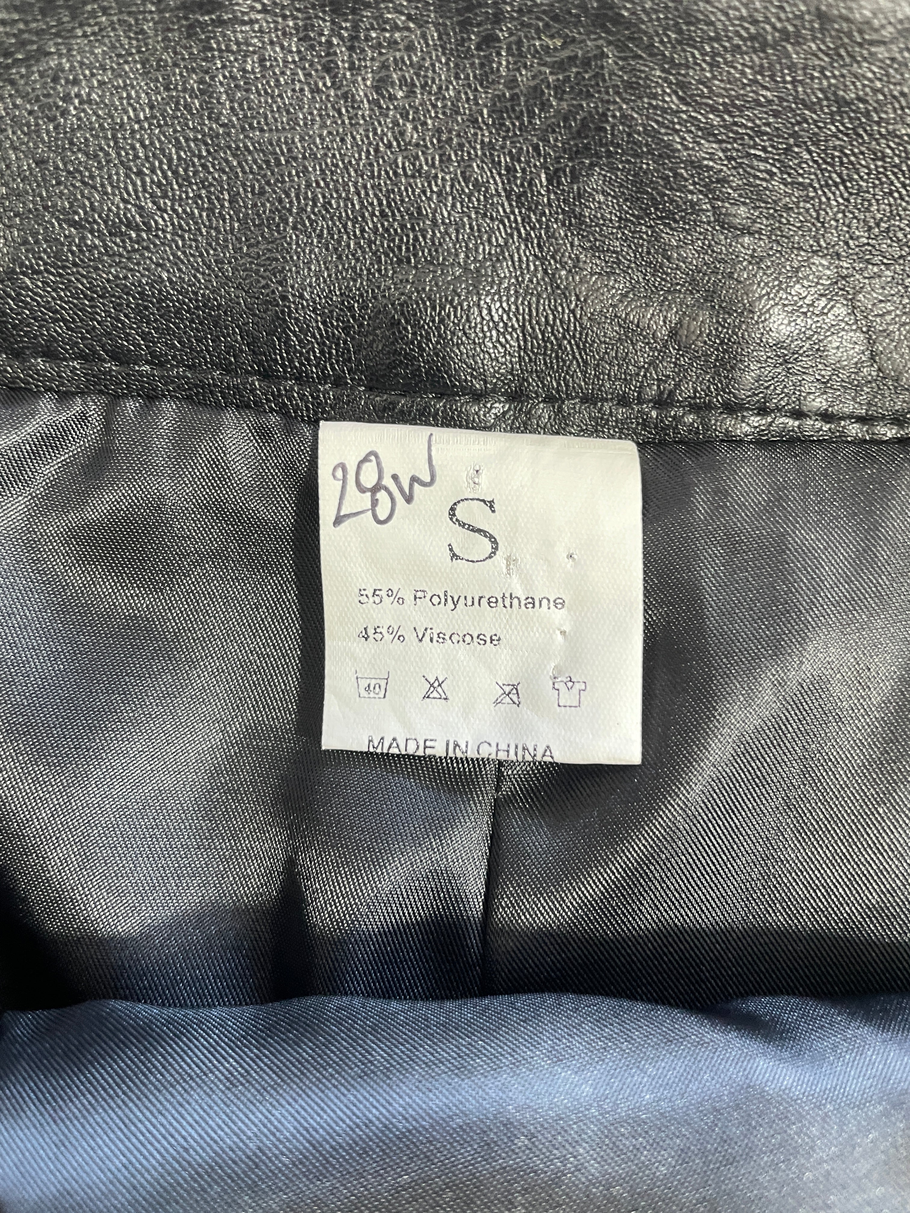 Close-up of a garment's interior neck label showing size 28W S with fabric composition details, set against a black textured outer lining and dark blue inner lining.