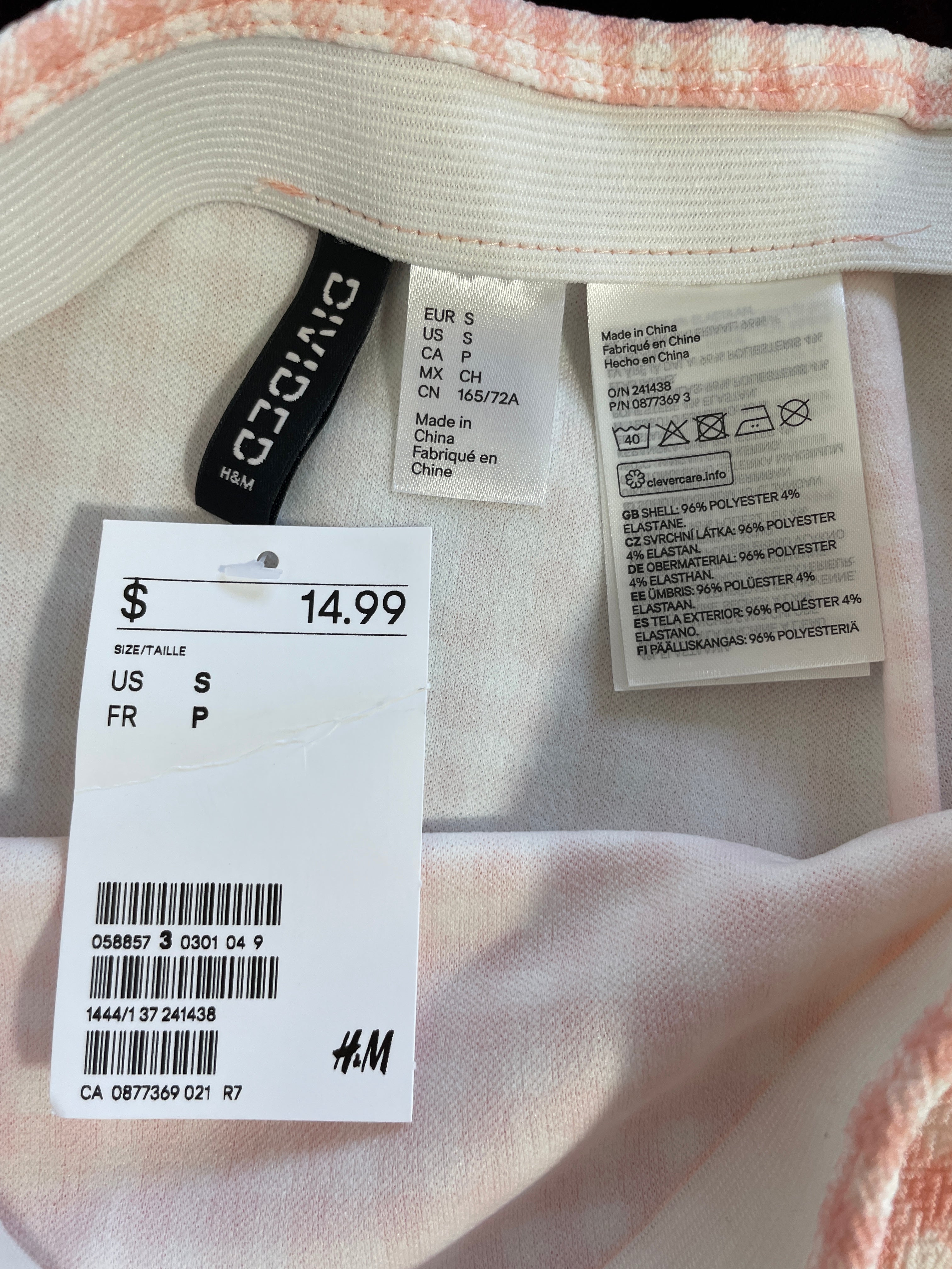 Close-up of the inside neckline of a pink and white striped garment, showing the H&M brand label, care instructions label, and a white price tag with the price $14.99.