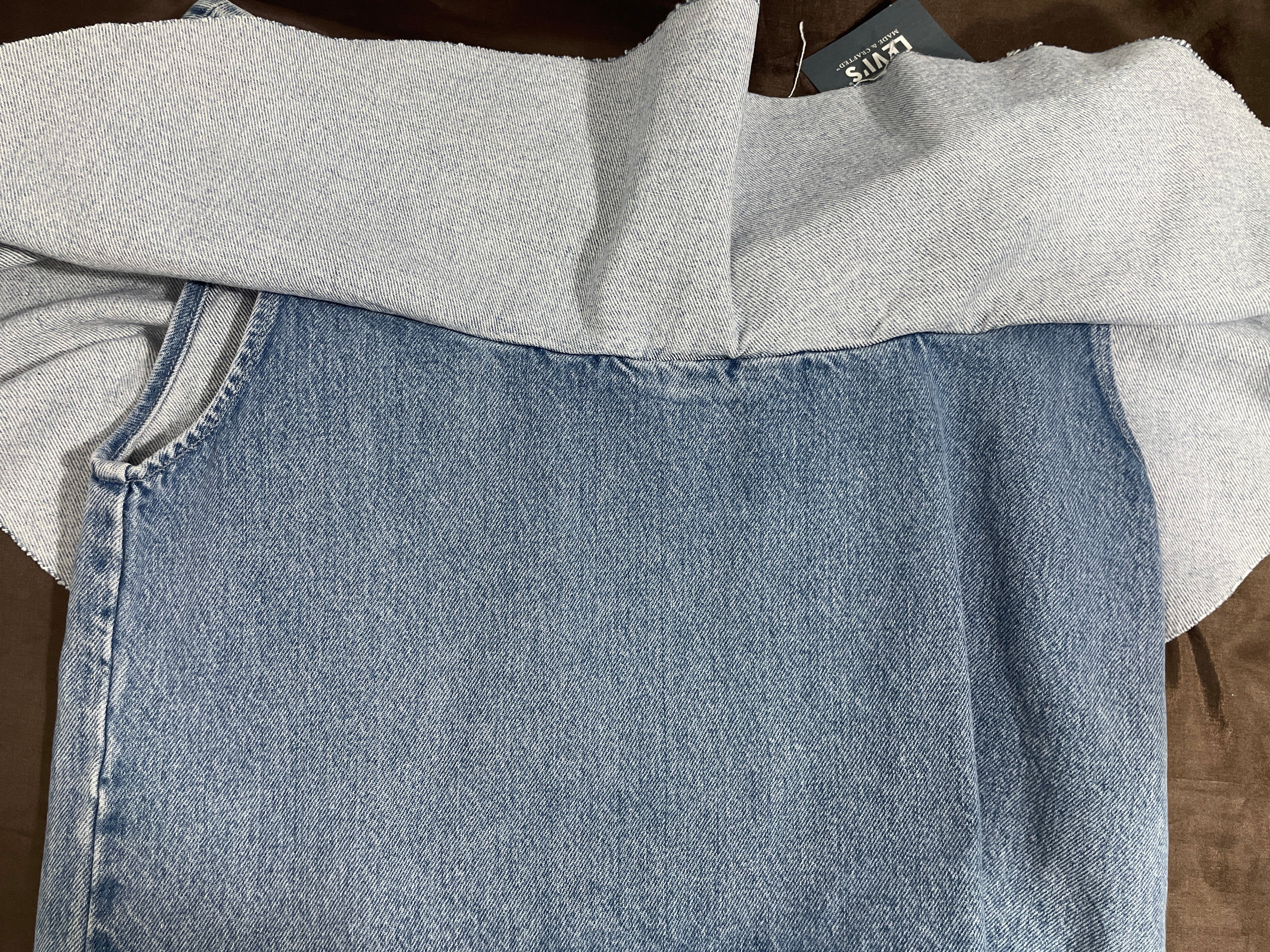 A folded light gray knit top or sweater layered over a light blue denim skirt, shown in a close-up flat lay on a brown surface. A gray H&M tag is visible at the collar.