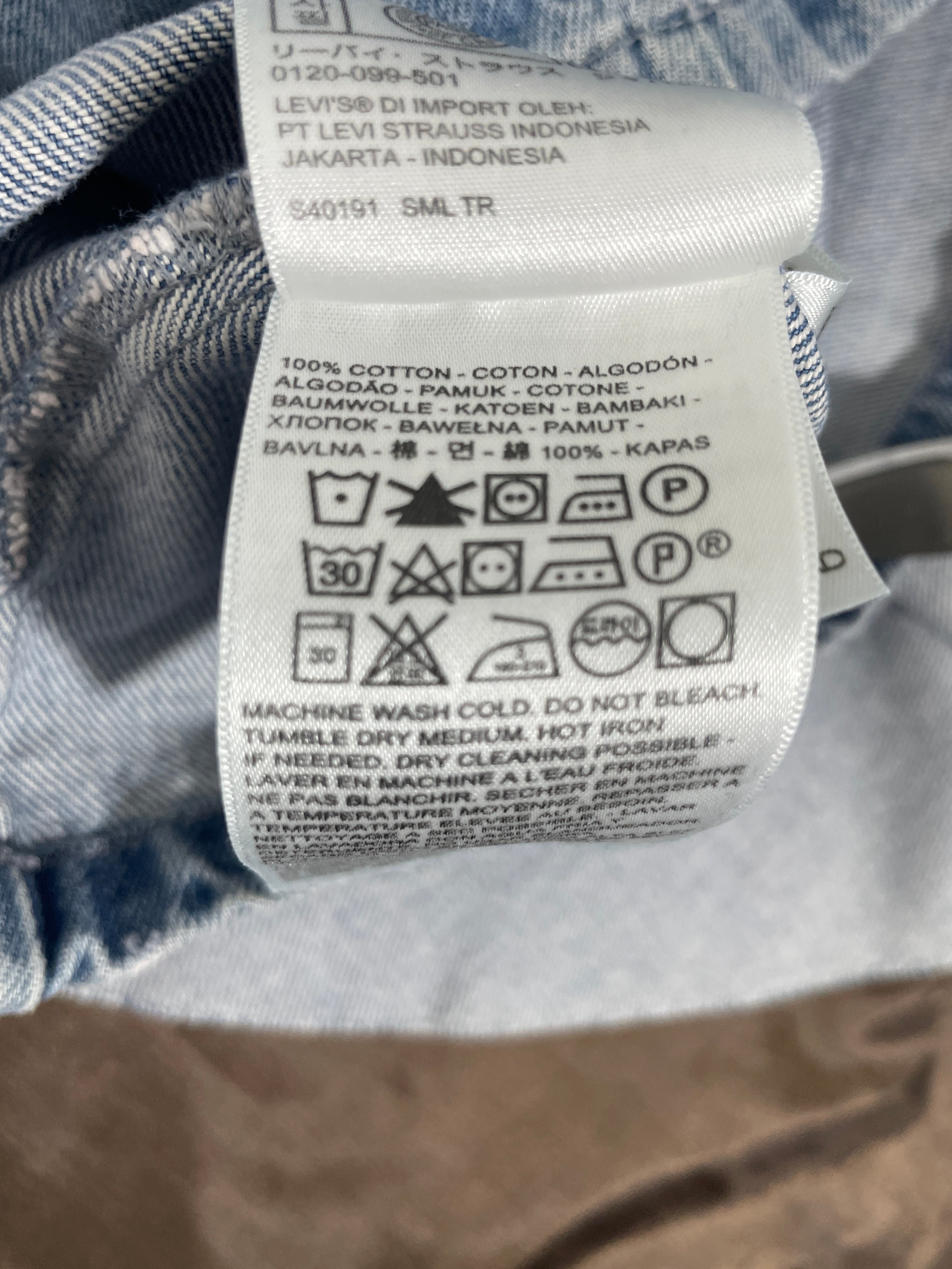 Close-up of a white garment care label sewn onto blue denim fabric, showing brand text and washing instructions.