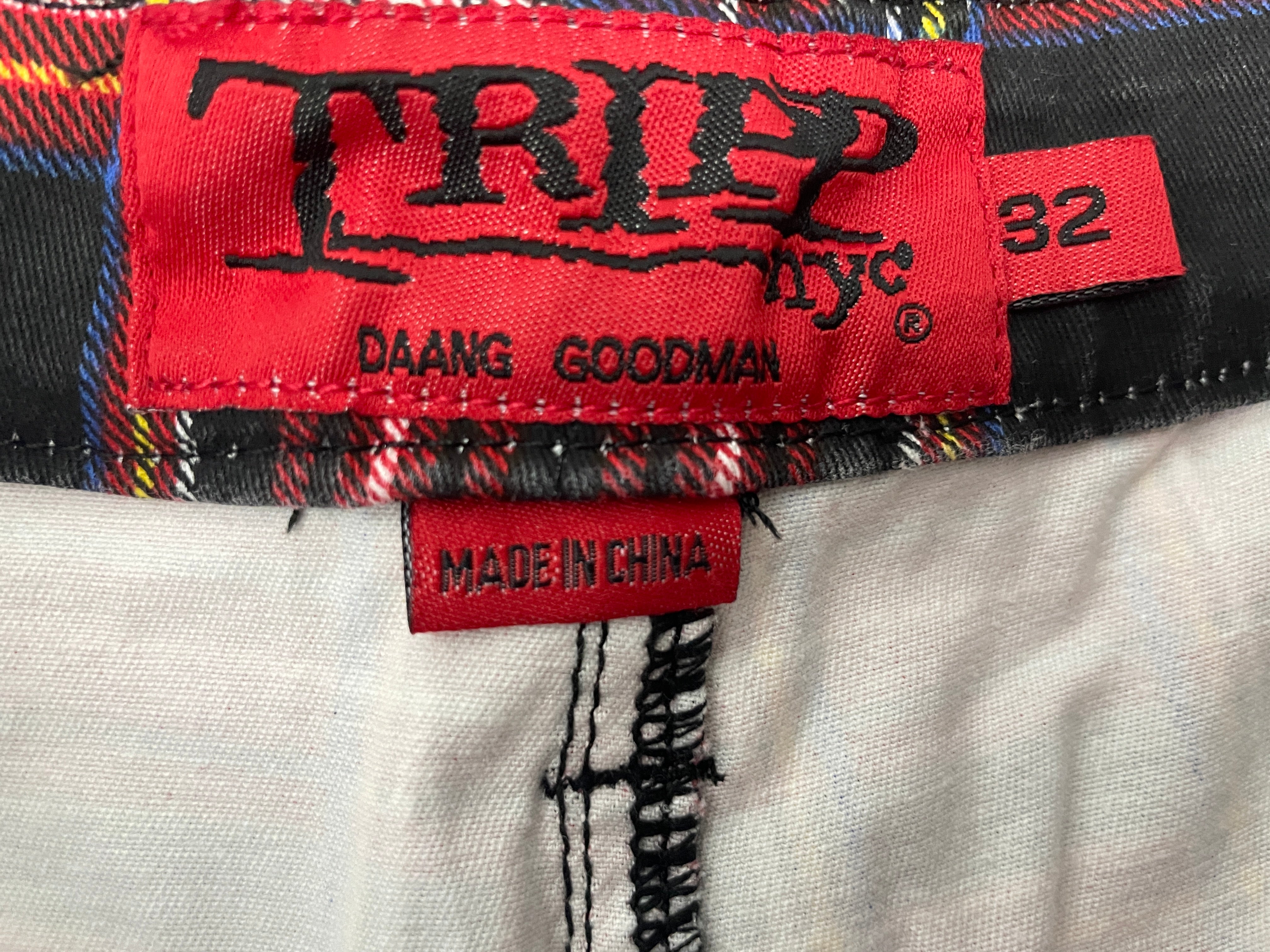 Close-up of a garment's interior labels showing a red 'TRIP' brand label and a smaller red 'MADE IN CHINA' tag, alongside a black and multicolor plaid fabric trim.