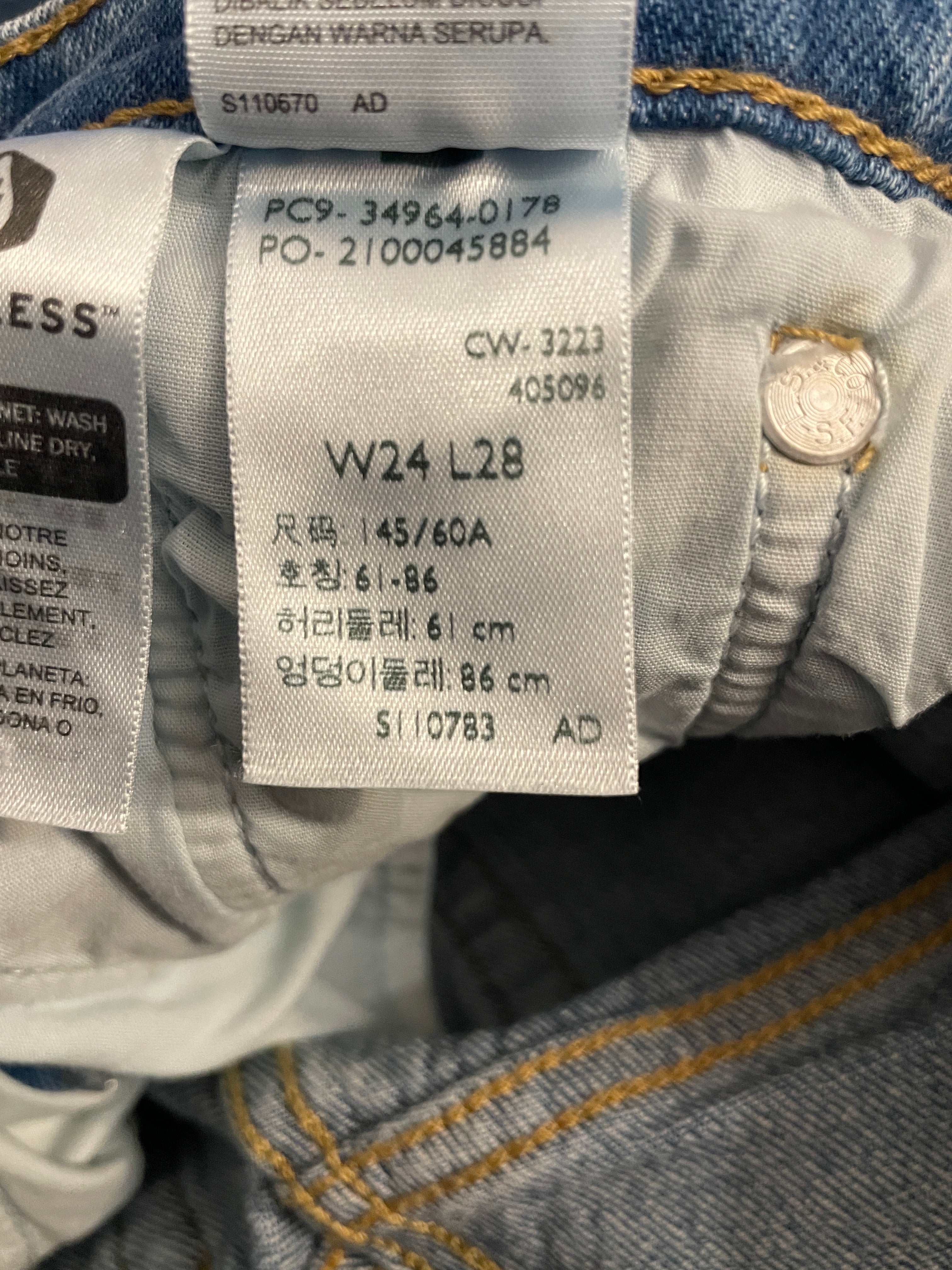 Close-up of a jeans inner label showing size information for a women's 34/60A size 61-86 fit, with blue denim fabric visible around it.