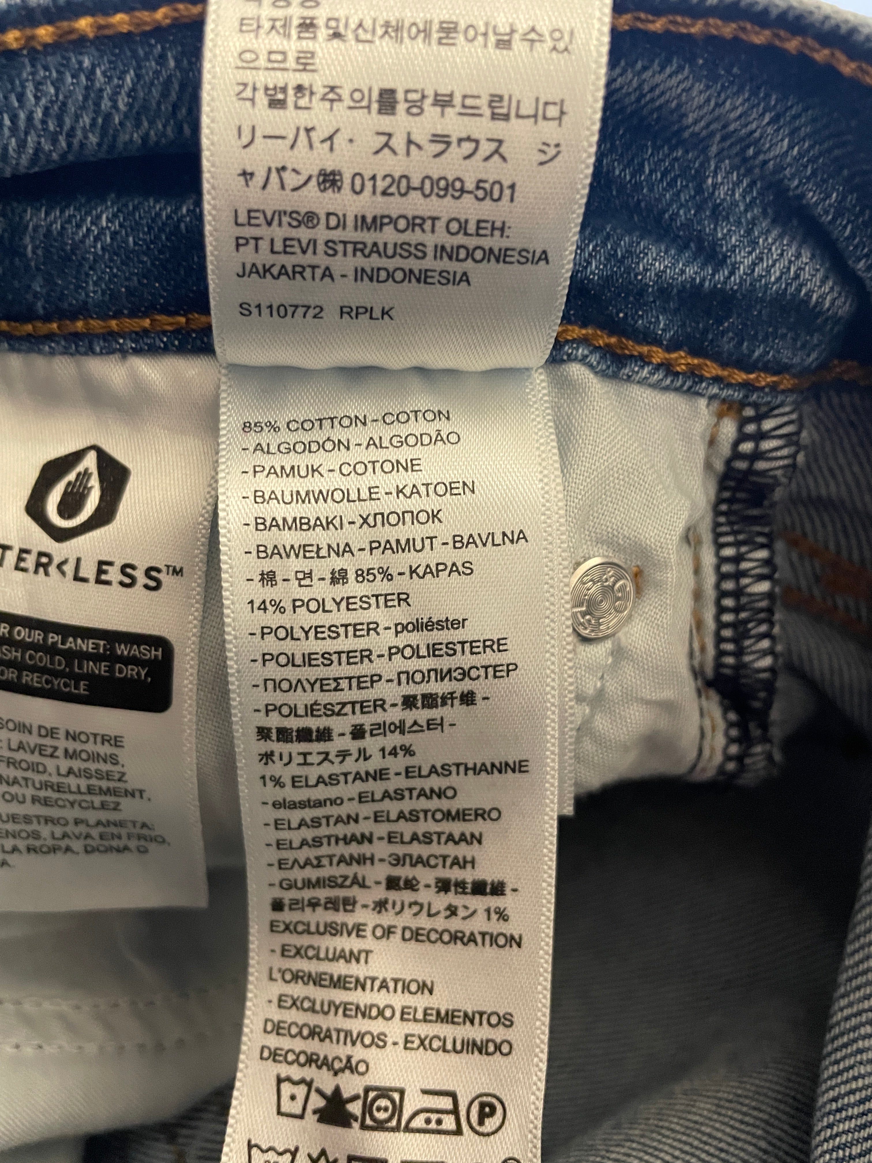Close-up of a white laundry care label sewn onto blue denim jeans, showing text including LEVI'S and care symbols.