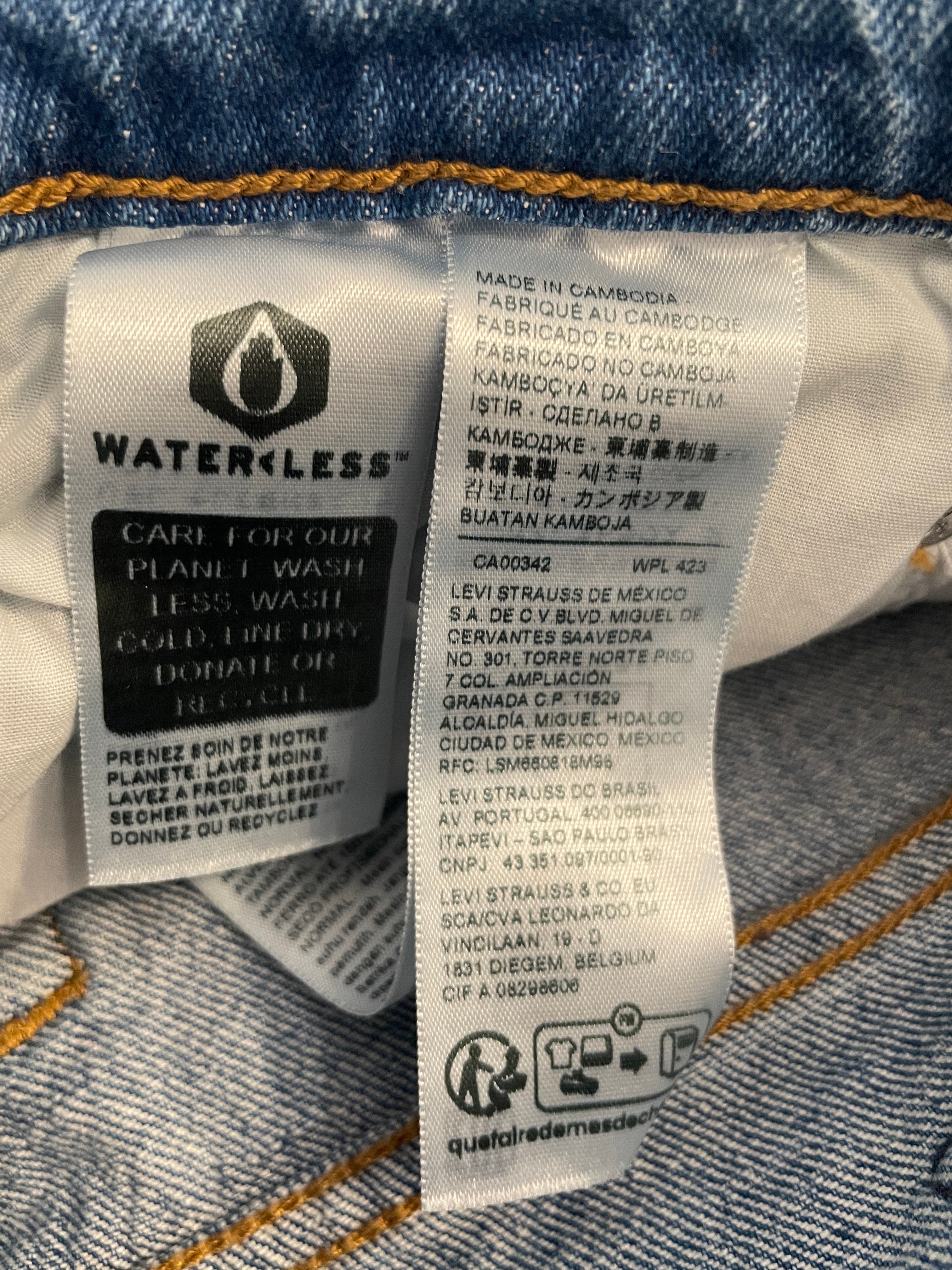 Close-up of a denim garment's interior care and product label, showing the Waterless Clean label and manufacturing details on a blue denim background.